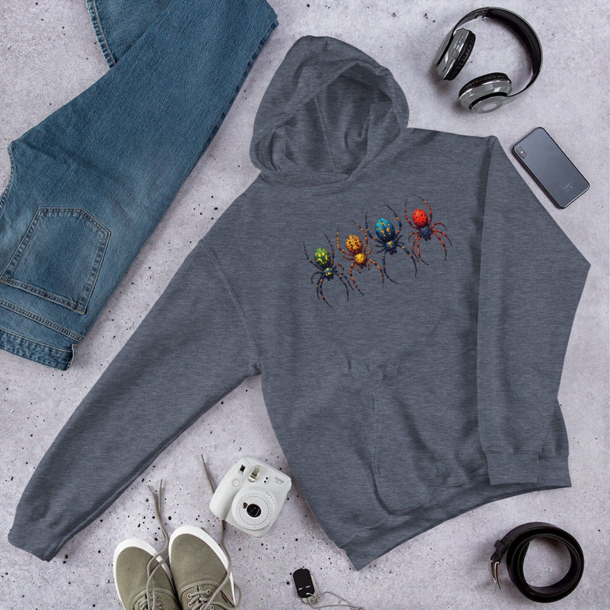 Gray hoodie with a colorful spider design on a gray surface with jeans, shoes, and accessories.