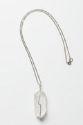 A silver-toned chain necklace with a large, irregular, clear crystal pendant, laid flat on a textured light gray fabric background.