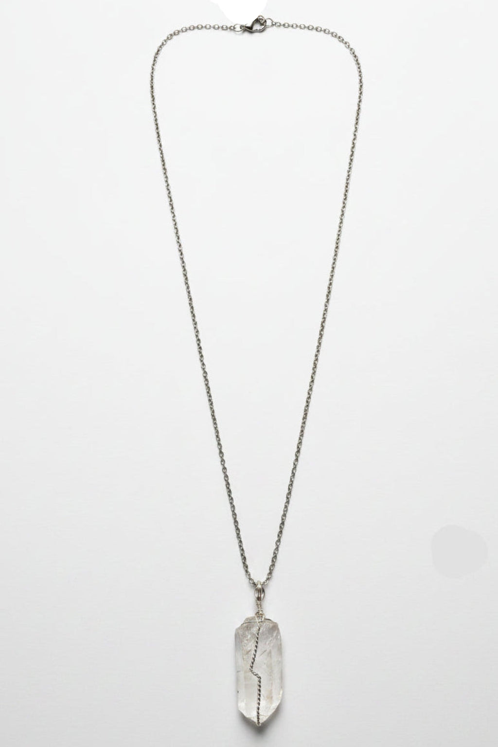 A silver-toned pendant necklace featuring a raw, polished crystal pendant, laid flat on a textured light gray fabric surface.