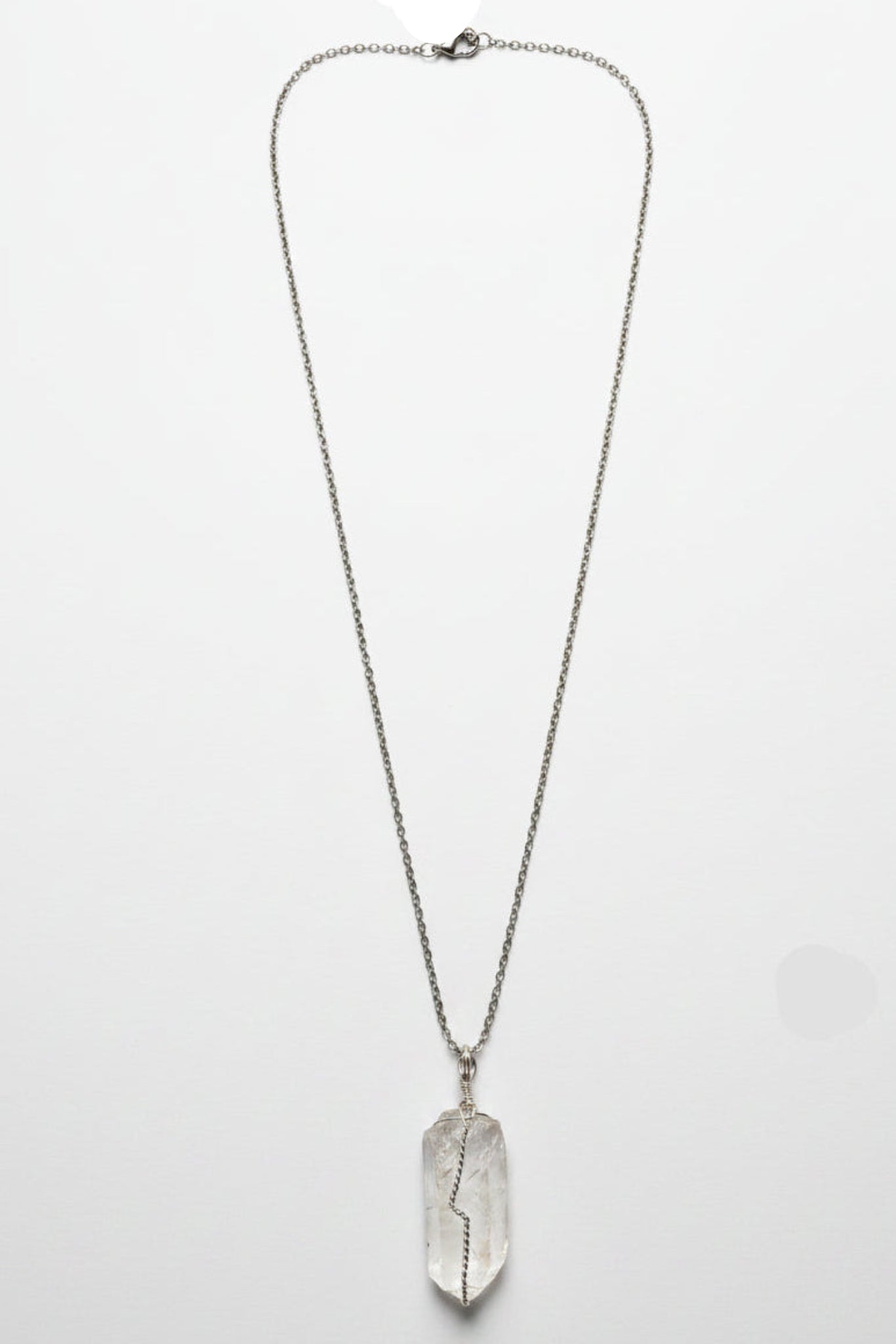 A silver-toned pendant necklace featuring a raw, polished crystal pendant, laid flat on a textured light gray fabric surface.