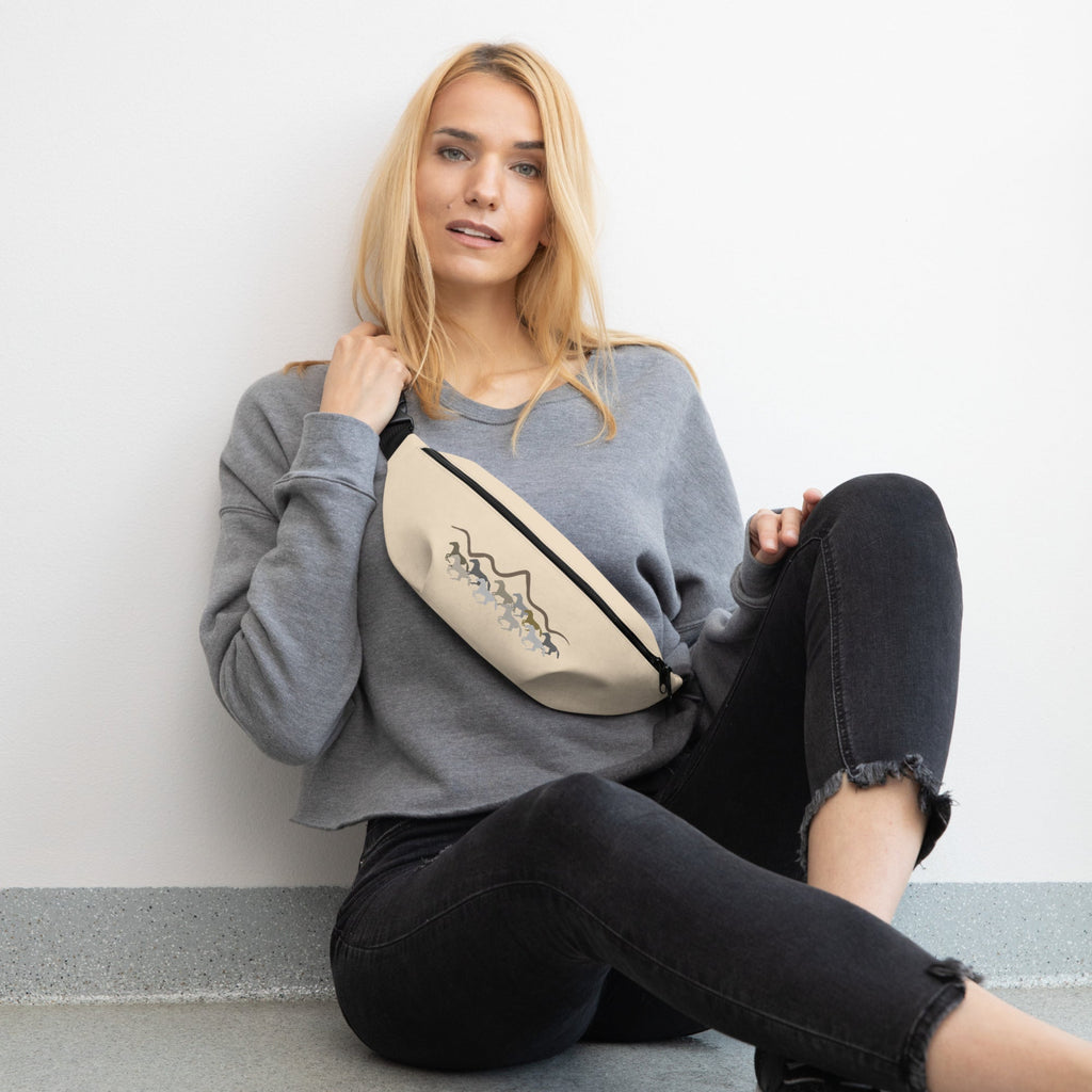 Woman sitting on the floor with a beige fanny pack with a wild mustangs and mountain design against a plain background.