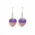 A pair of heart-shaped dangle earrings made from translucent purple and pink resin, suspended from silver fishhook wires on a plain white background.