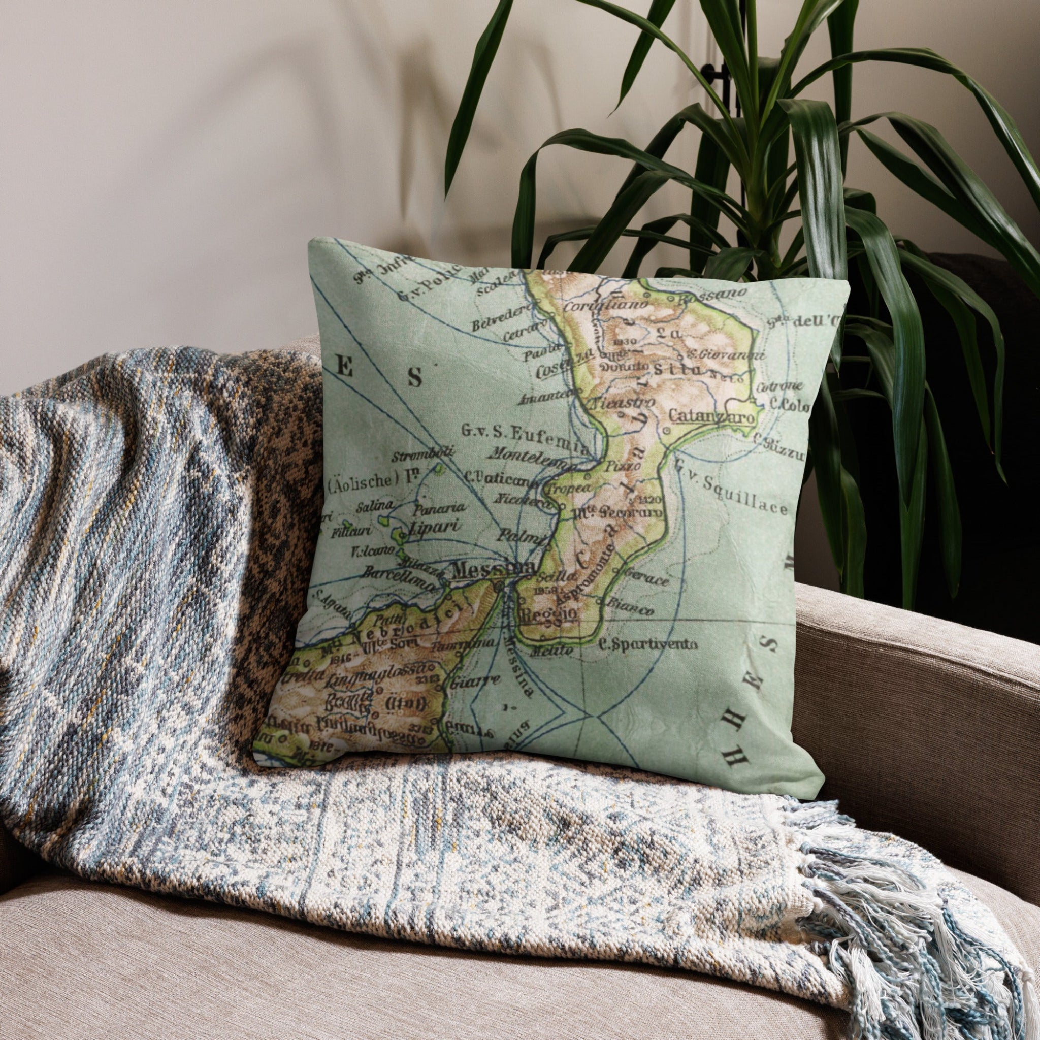 Map pillow on a textured blanket with a plant in the background