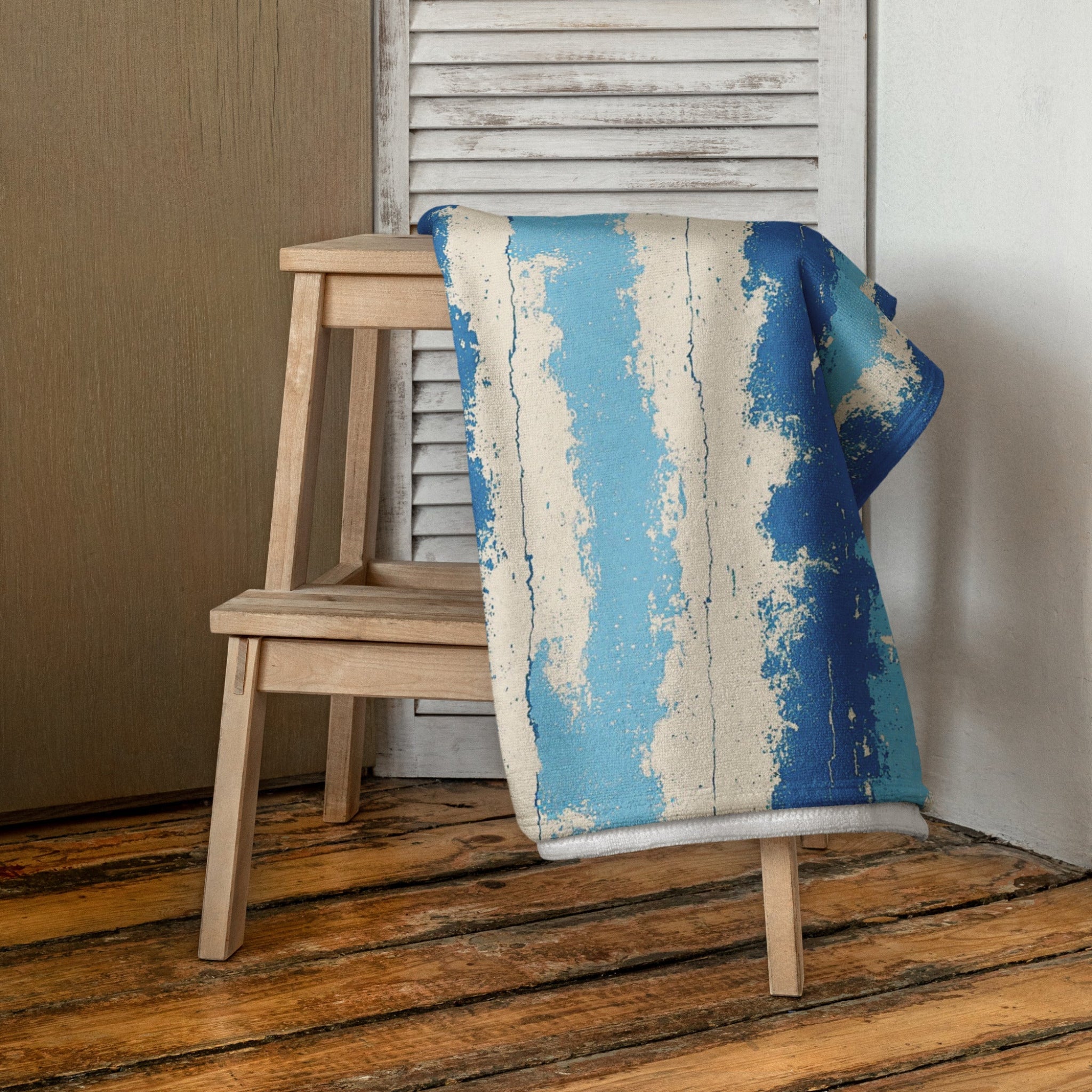 Blue and beige patterned towel draped over a wooden stool against a neutral wall.