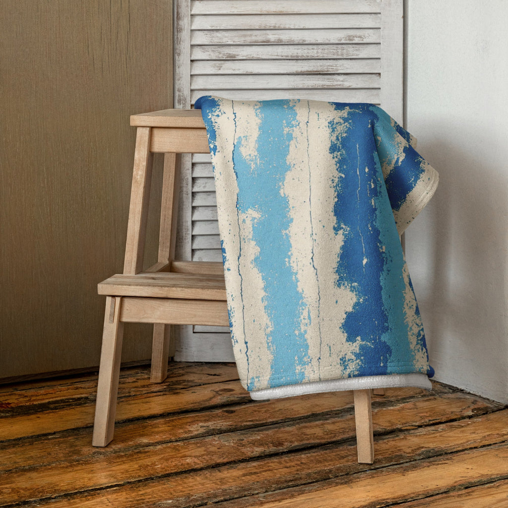 Blue and beige patterned blanket draped over a wooden chair against a neutral wall.