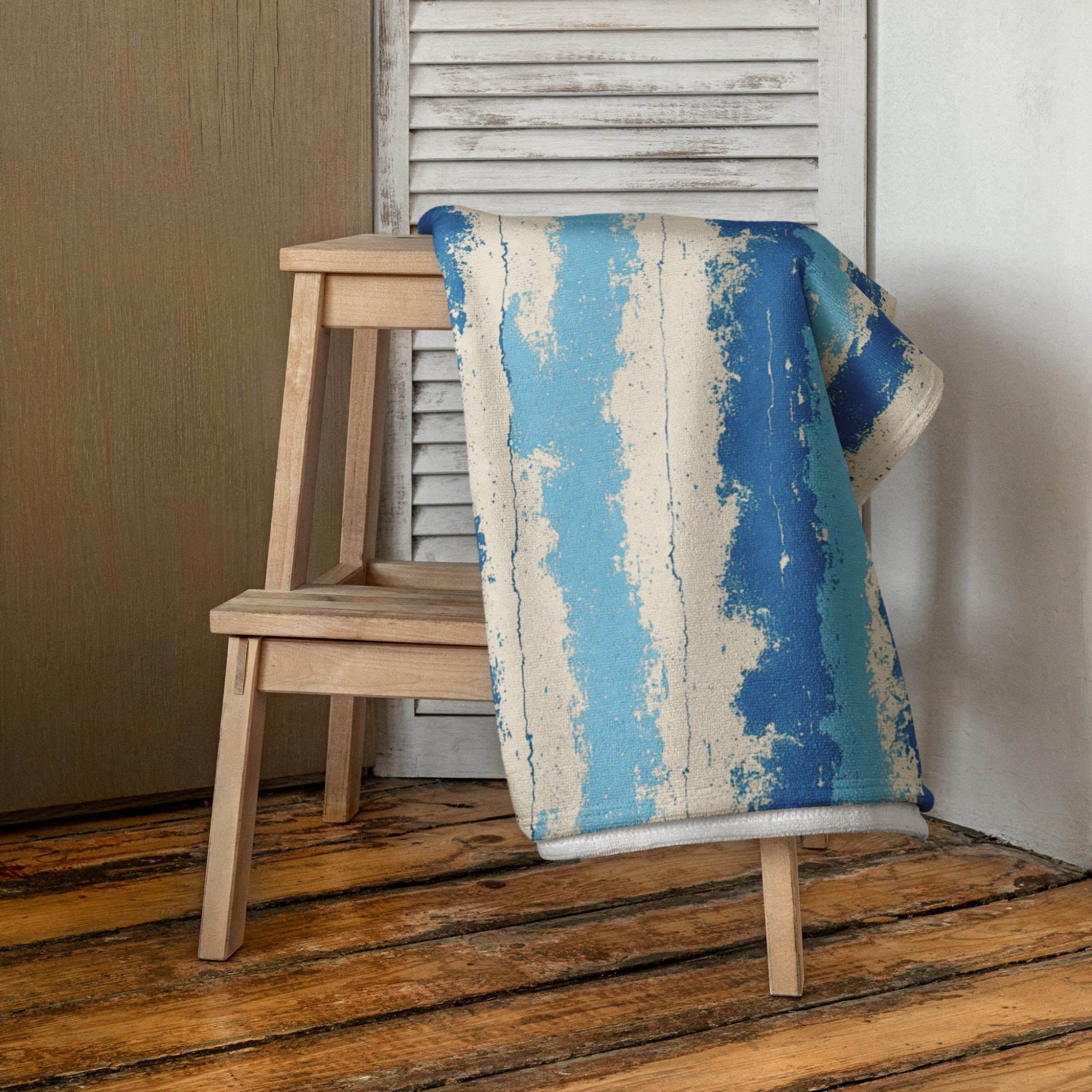 Blue and beige patterned blanket draped over a wooden chair against a neutral wall.