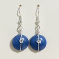 A pair of handmade dangle earrings featuring round, glittery blue beads suspended from silver hooks with twisted wire details, displayed on a brown textured surface.