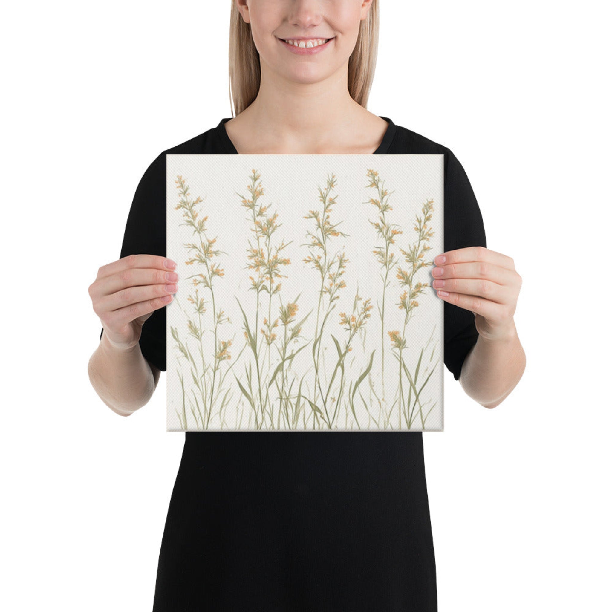 A a woman holding a square canvas print featuring minimalist illustrations of delicate, neutral-toned meadow grasses and wildflower stems on a cream background
