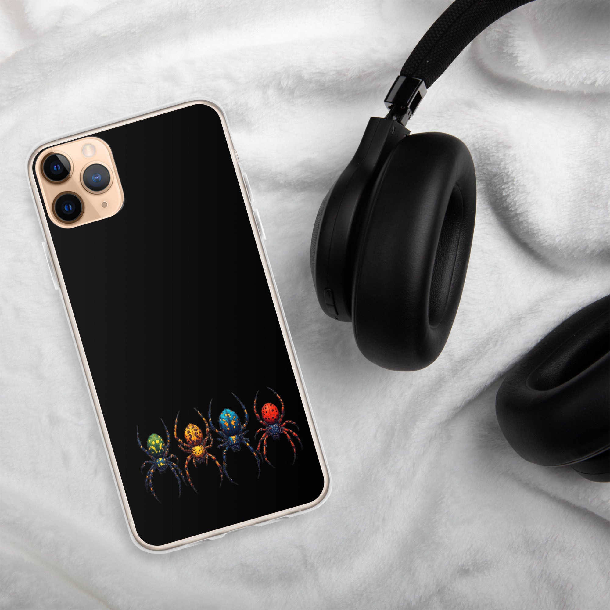 A black phone case with a colorful spider graphic, shown on a smartphone next to black headphones on a white textured blanket background.
