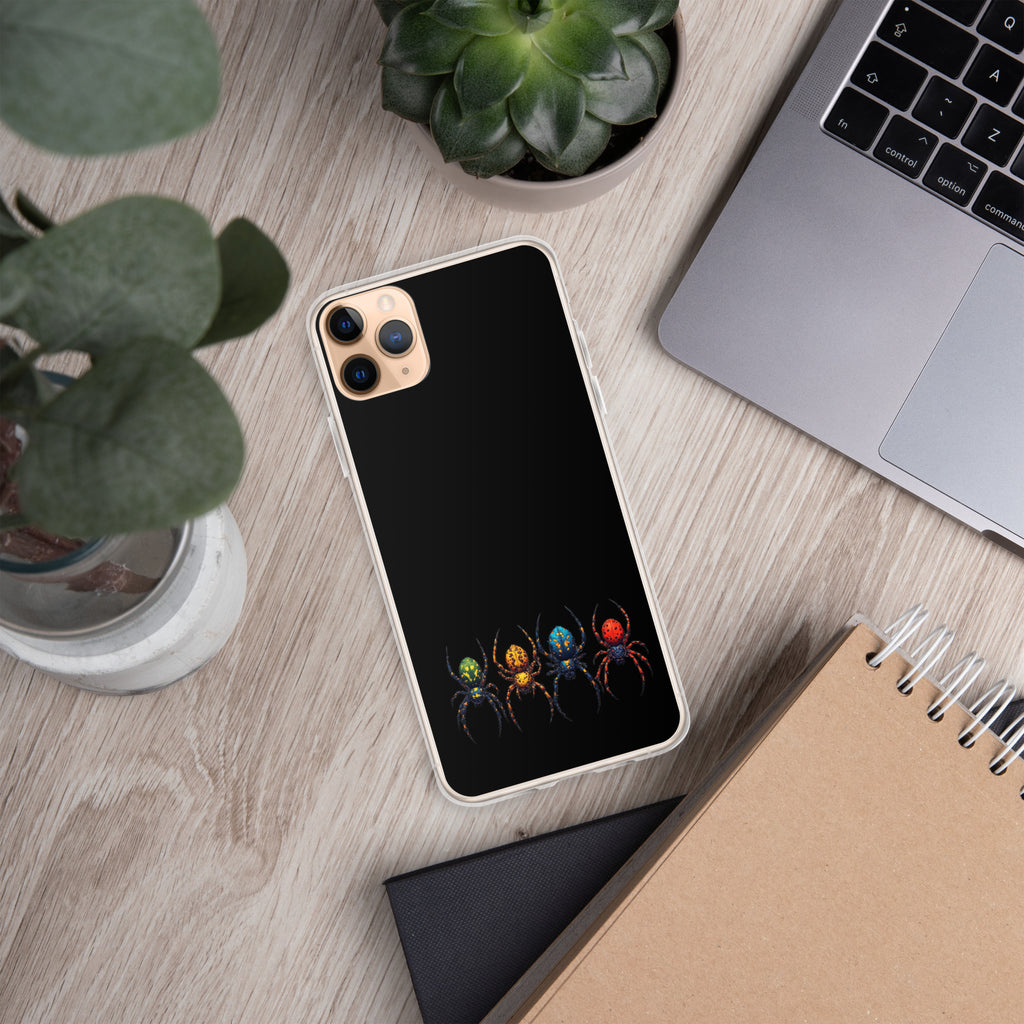 A black phone case with a colorful spider design, shown on a silver smartphone, placed on a light wood desk with a laptop, plants, and a notebook nearby.