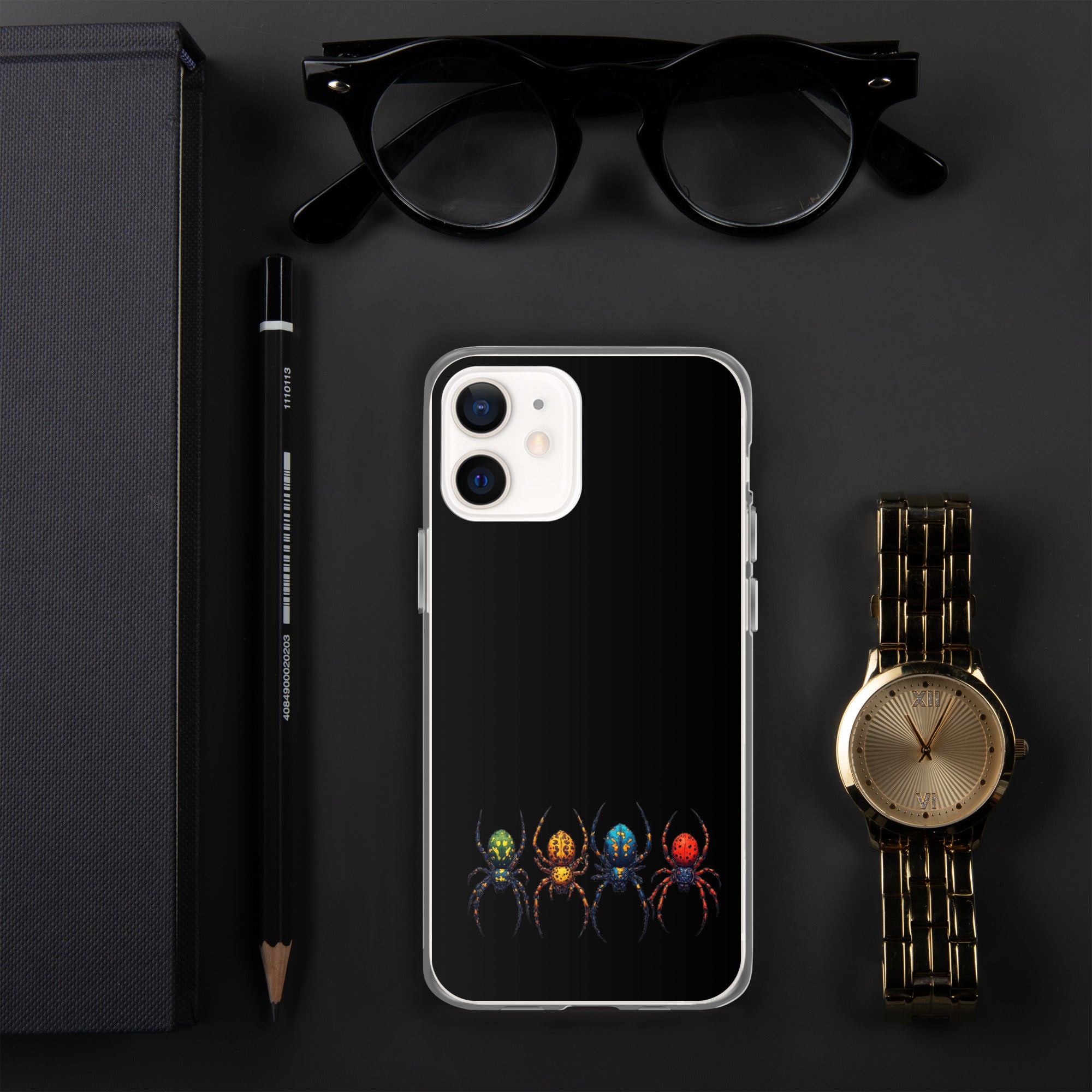 A black phone case with a colorful spider graphic, displayed in a flat-lay arrangement with black eyeglasses, a black pencil, a gold watch, and a dark gray notebook on a dark gray background.