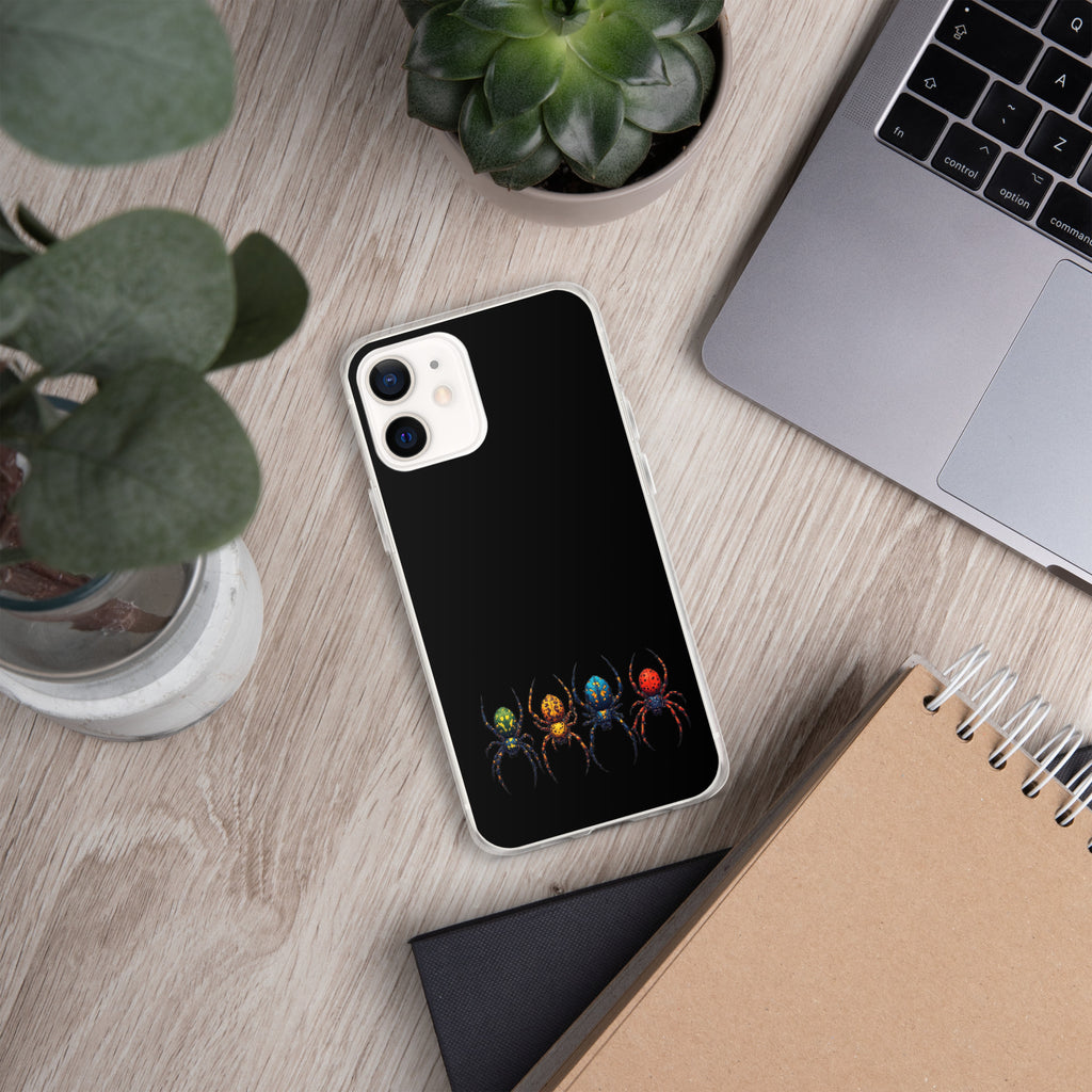 A black phone case with a graphic of three colorful spiders at the bottom, shown on a light wood desk with a laptop, plants, and a notebook.