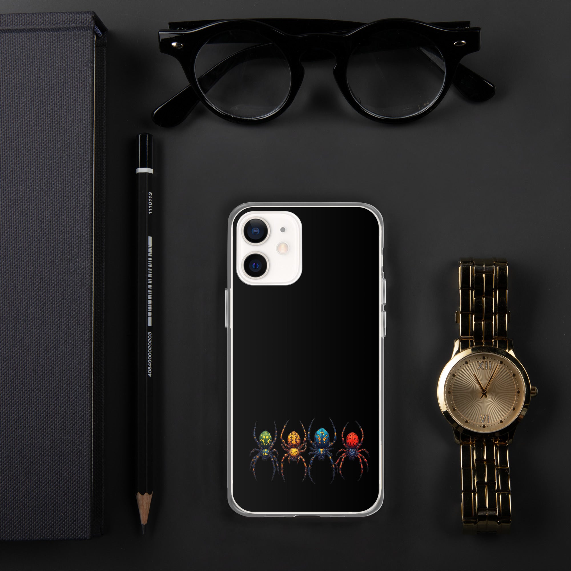 A black phone case with a colorful spider graphic, displayed in a flat-lay arrangement with black eyeglasses, a black pencil, a gold watch, and a black notebook on a dark gray background.