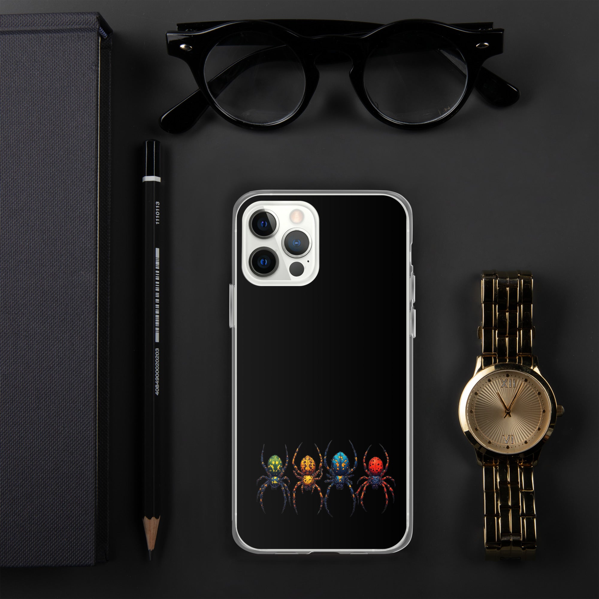 A clear phone case with a black back panel printed with four colorful spiders at the bottom, shown in a styled flat-lay with black eyeglasses, a black pencil, a gold-tone watch, and a dark box on a dark gray background.