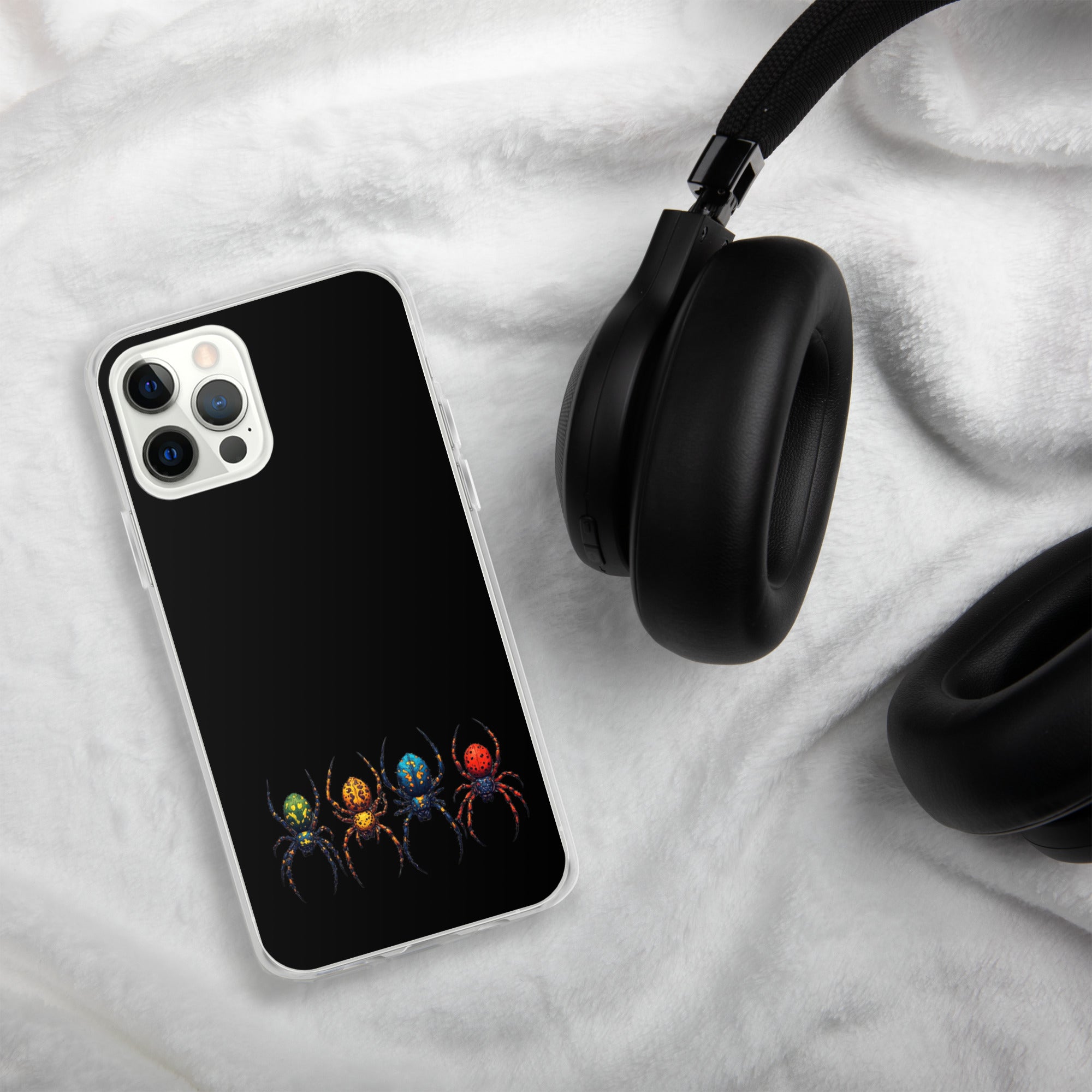 A black phone case with a colorful spider graphic, shown on a white plush blanket next to black headphones.