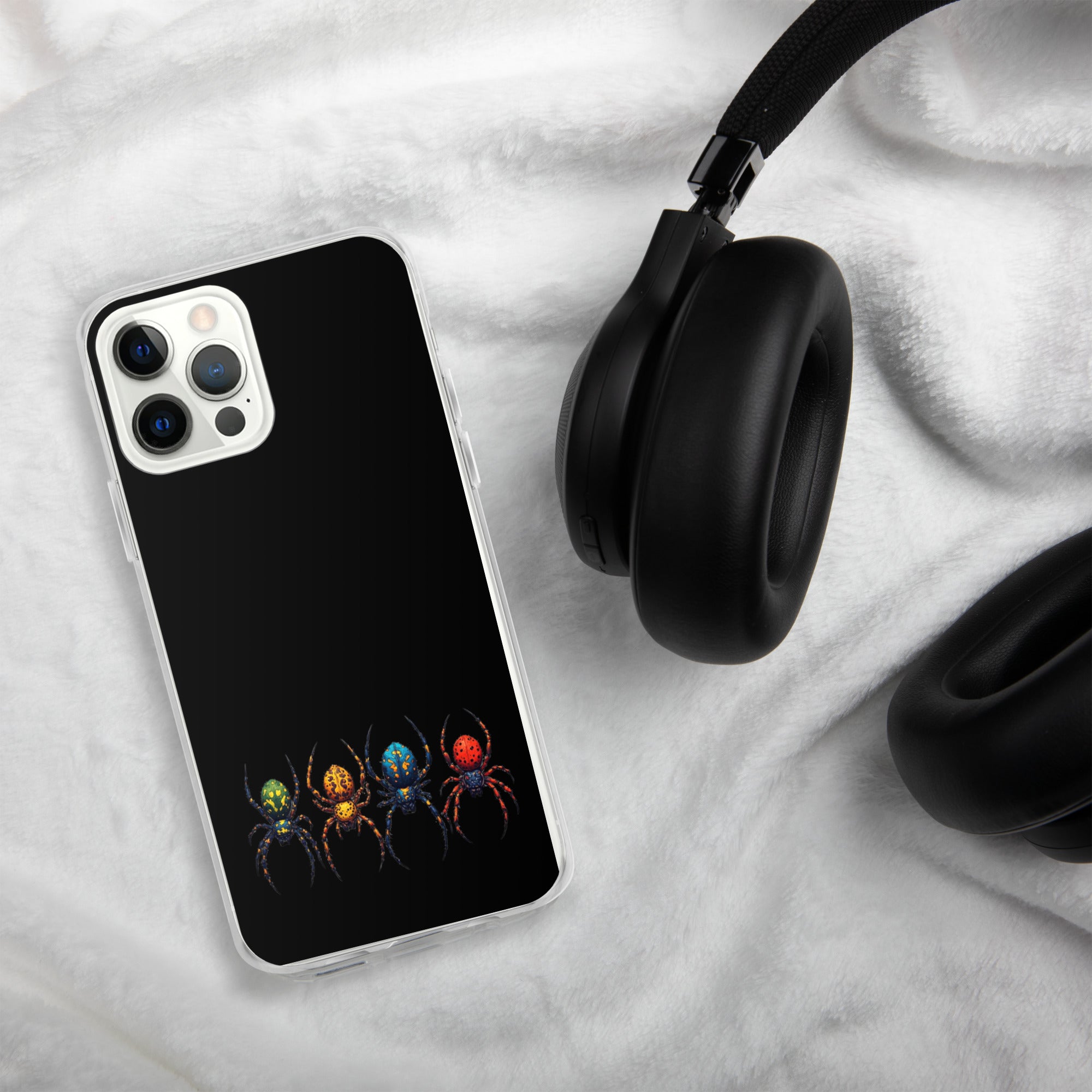 A black phone case with a colorful spider graphic, shown on a smartphone next to black headphones on a white textured blanket background.