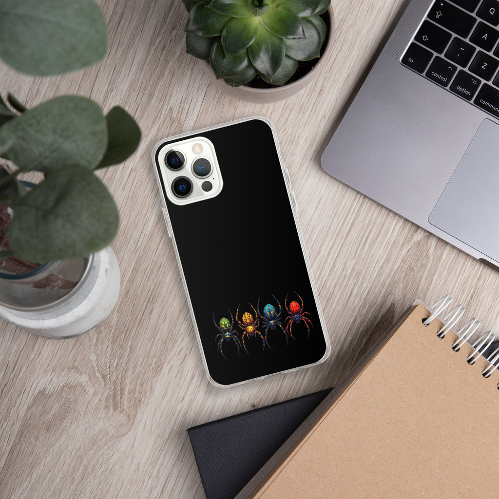 A black phone case with a graphic of four colorful spiders, shown on a silver smartphone. The phone case is displayed in a styled flat-lay setting on a light wood desk alongside a laptop, plants, and notebooks.