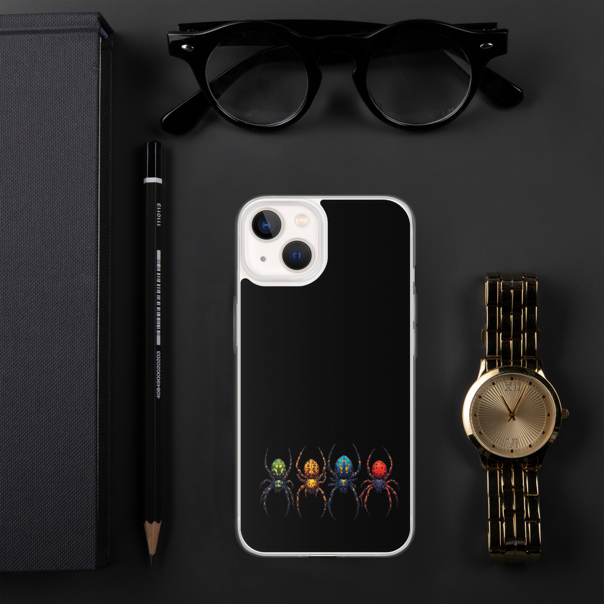 A black phone case with a colorful spider design, displayed in a flat-lay arrangement with black eyeglasses, a black pencil, a black notebook, and a gold watch on a dark gray background.