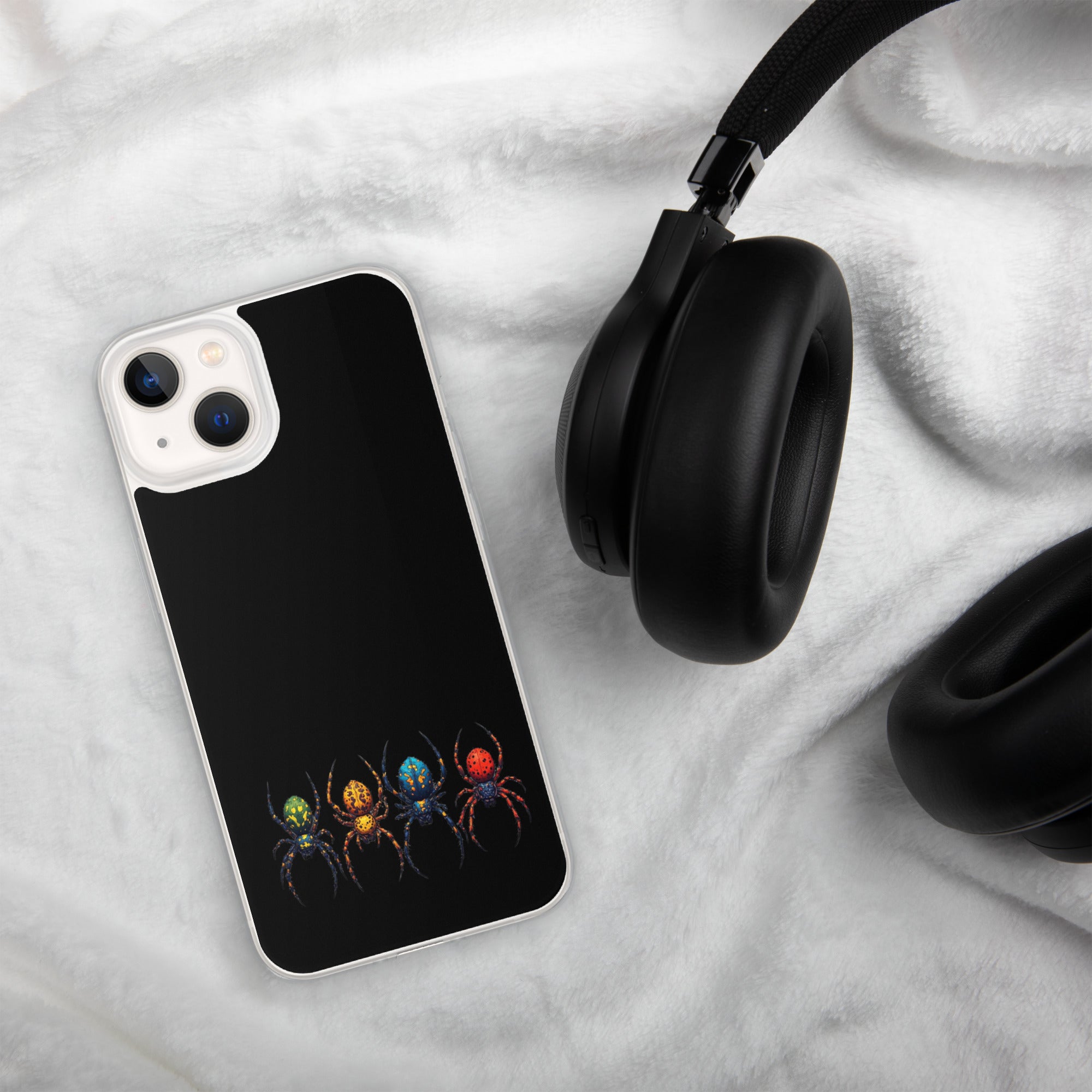 A black phone case with a graphic of four colorful spiders in green, orange, blue, and red, shown on a white plush blanket next to black headphones.