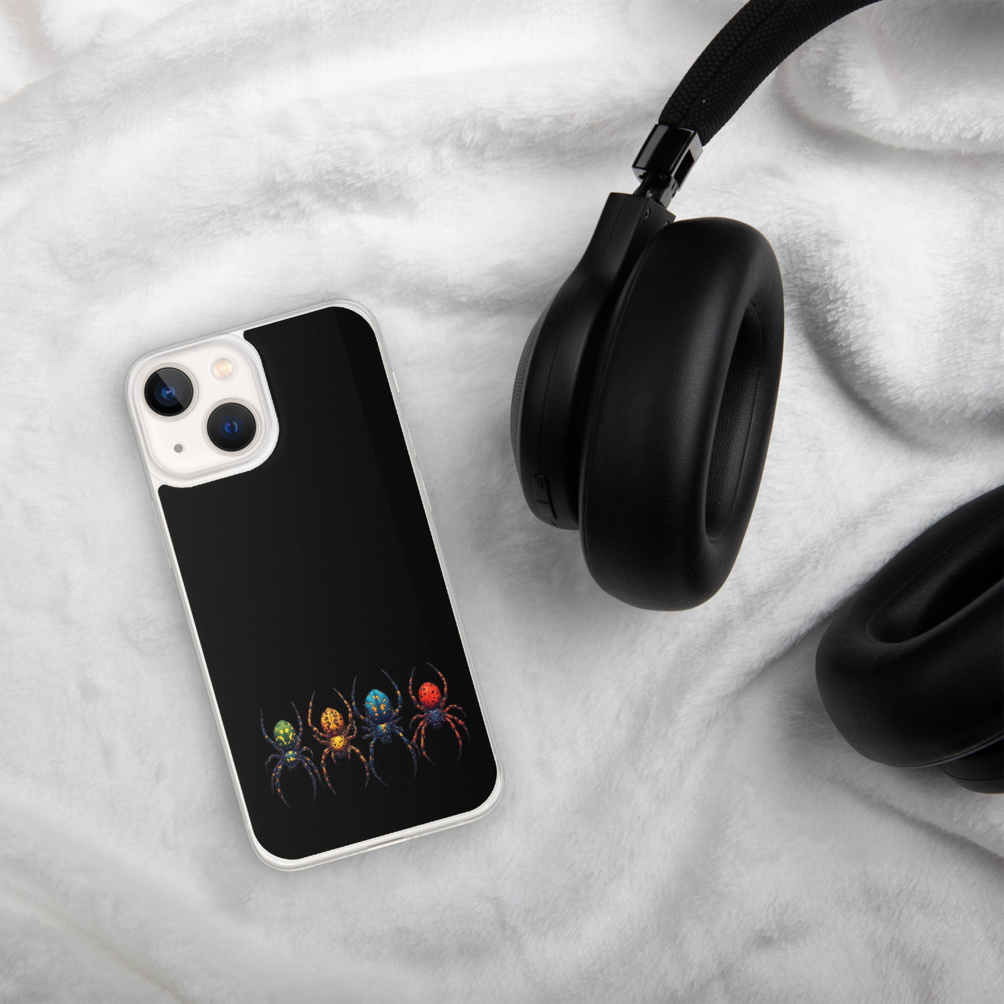 A black phone case with a colorful spider graphic, shown on a white textured blanket next to black headphones.