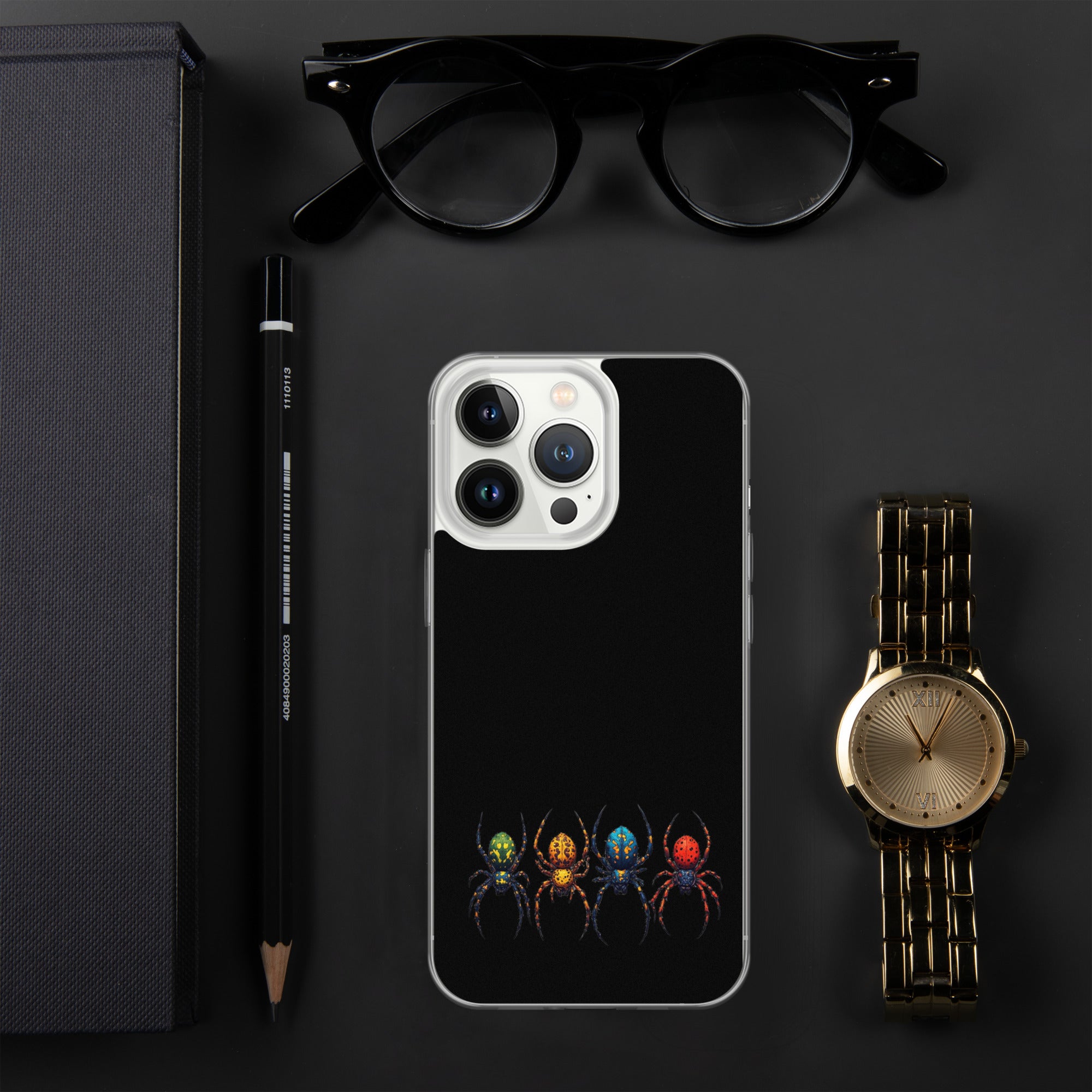 A black phone case with a colorful spider graphic, displayed in a styled flat-lay arrangement with black eyeglasses, a black pencil, a gold watch, and a dark textured box on a dark gray background.