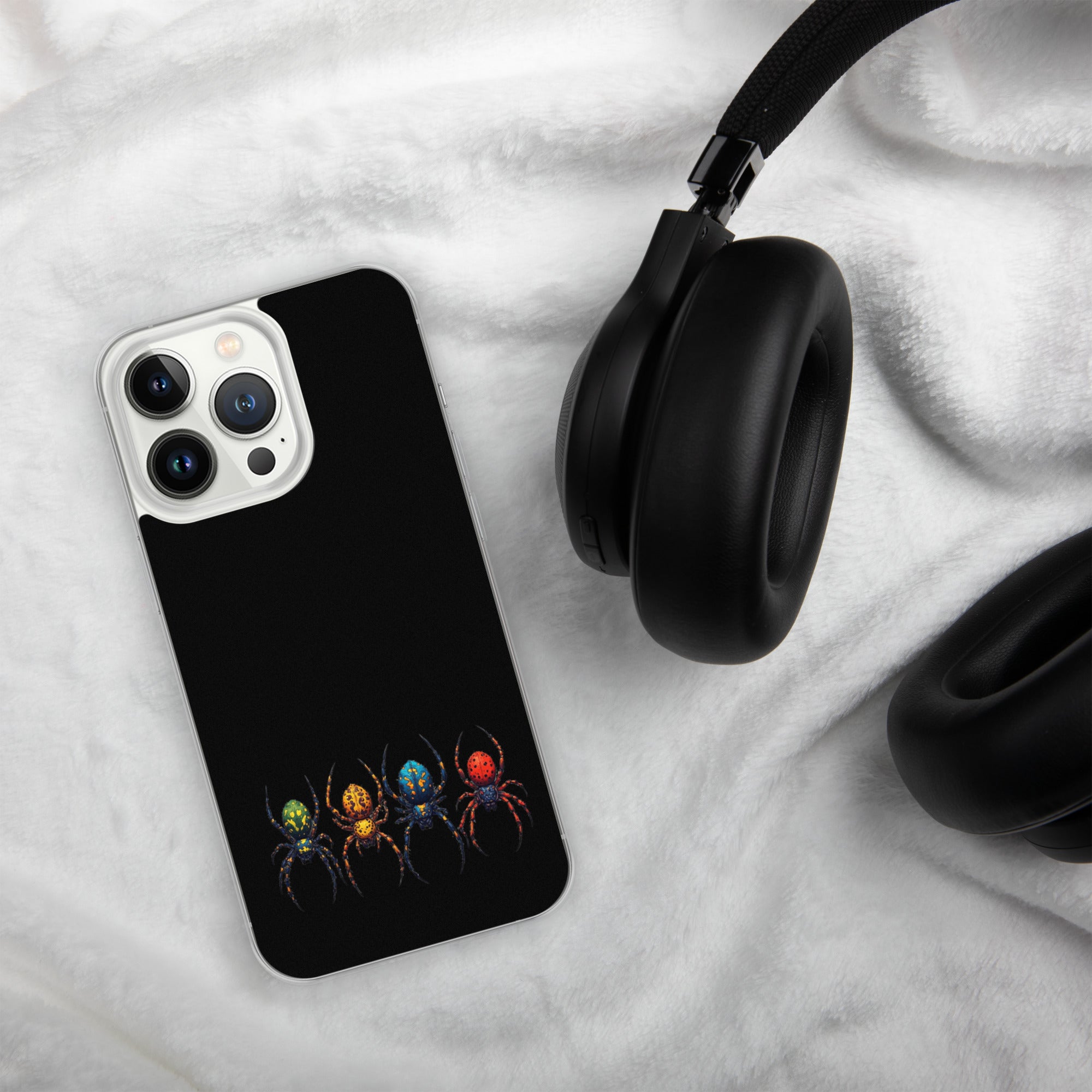 A black phone case featuring a colorful graphic of four stylized spiders in green, orange, blue, and red, shown on a white textured blanket next to black headphones.