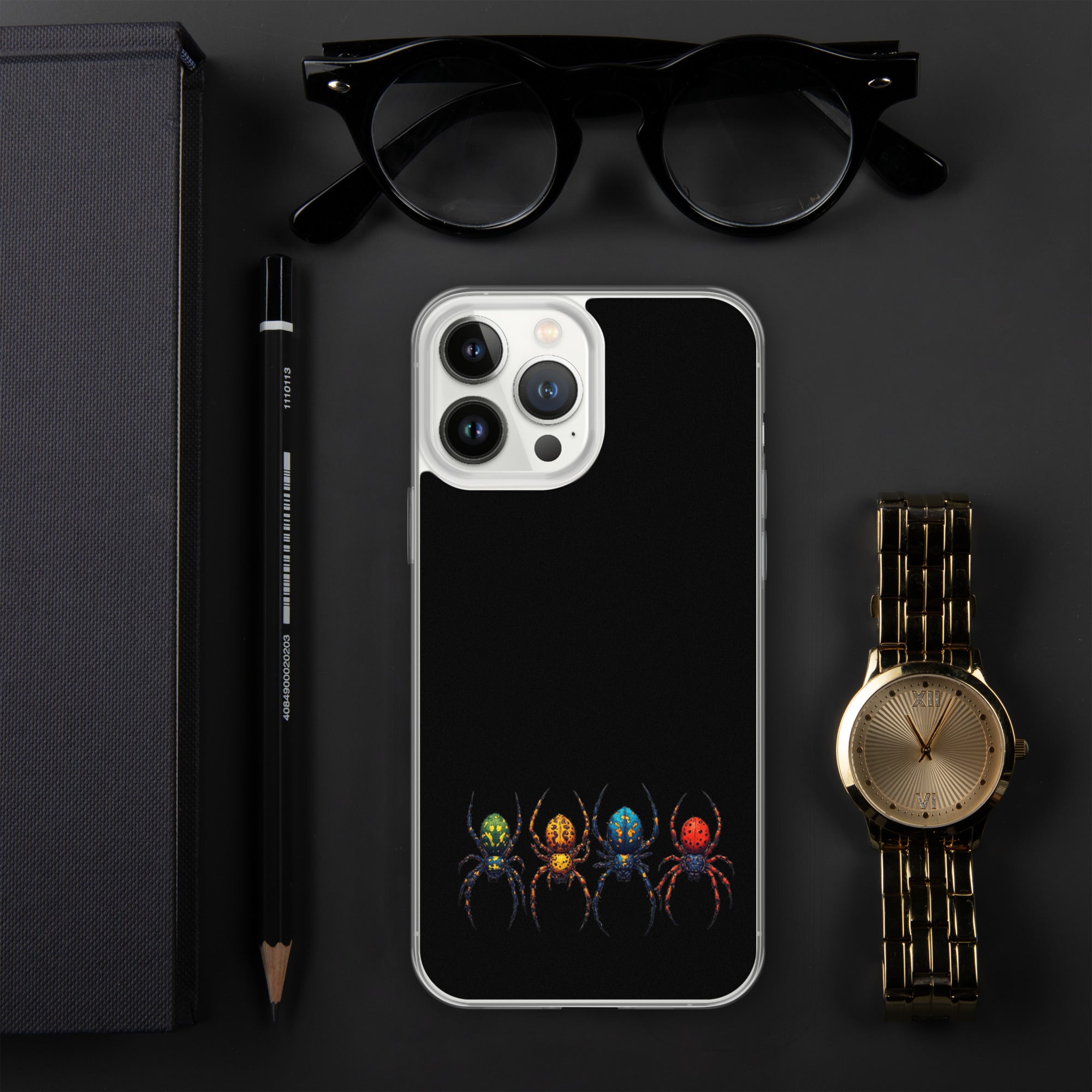 A black phone case with a colorful spider graphic, displayed in a flat-lay arrangement with black eyeglasses, a black pencil, a gold watch, and a black notebook on a dark gray background.