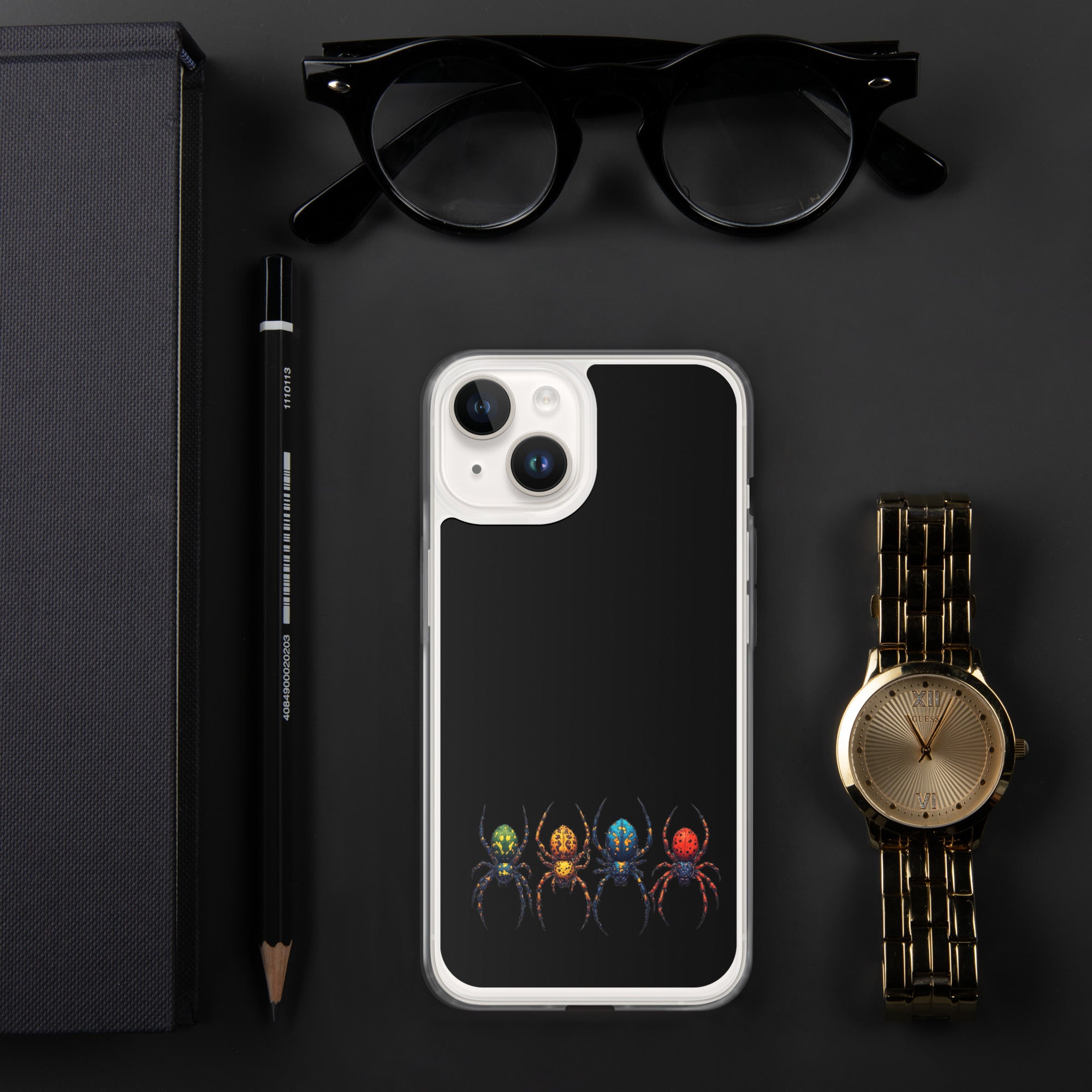 A phone case with a black back featuring a colorful spider illustration, shown in a styled flat-lay with black eyeglasses, a black pencil, a gold watch, and a dark textured box on a dark gray background.
