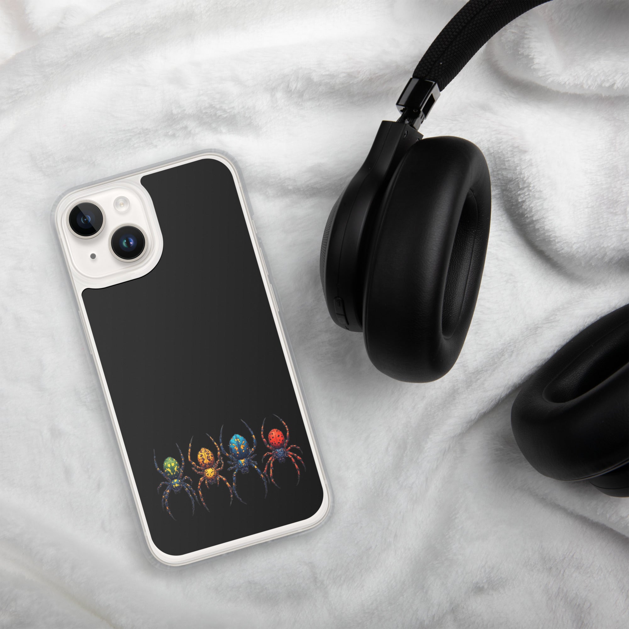 A smartphone case with a black back and a colorful spider print near the bottom, shown on a white plush blanket next to black headphones.