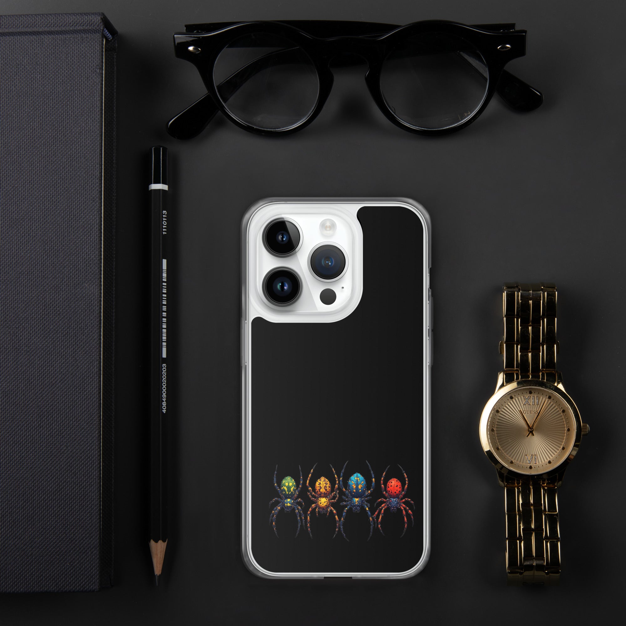 A clear phone case with a black back panel featuring a graphic of four colorful spiders at the bottom, styled in a flat-lay with black eyeglasses, a black pencil, a black notebook, and a gold-tone watch on a dark gray background.