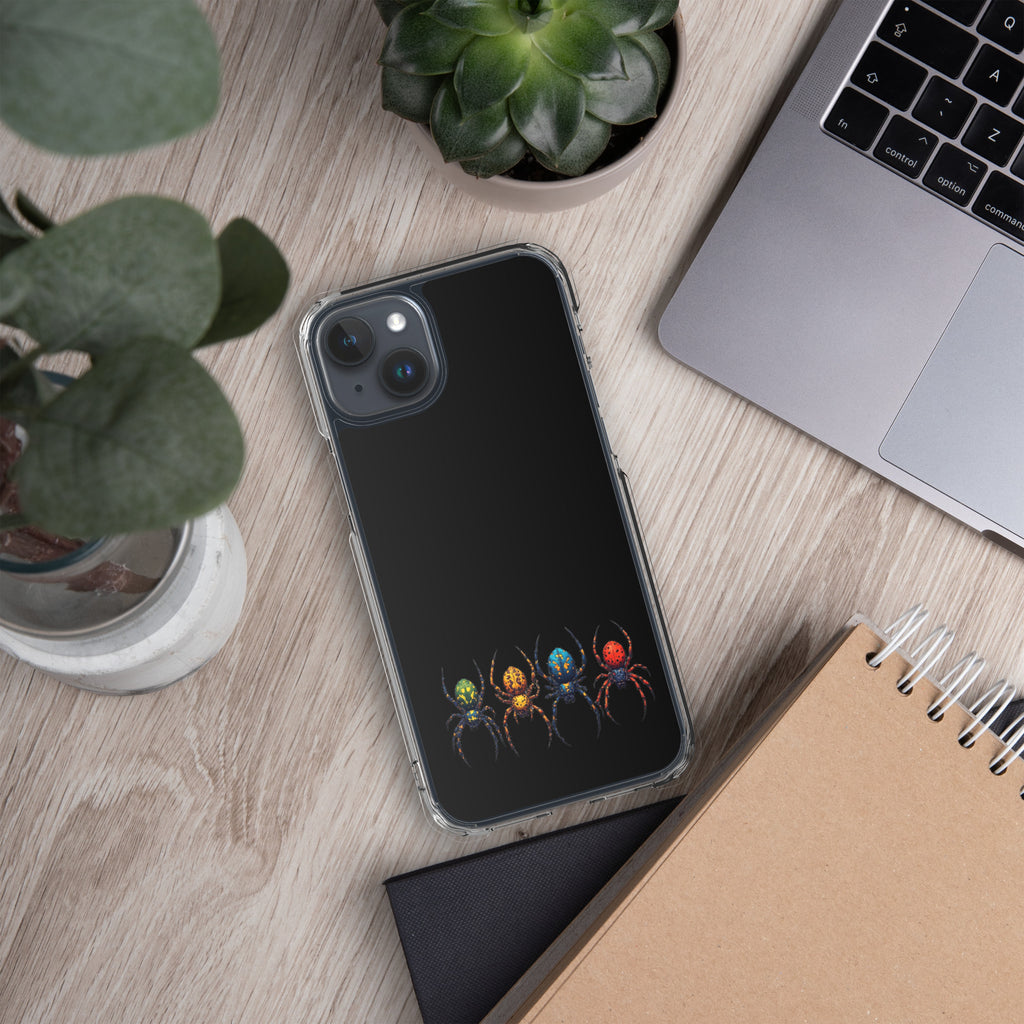 A clear-edged smartphone case with a black back panel and a printed design of four colorful spiders, shown on a light wood desk with a laptop, notebook, and plants nearby.