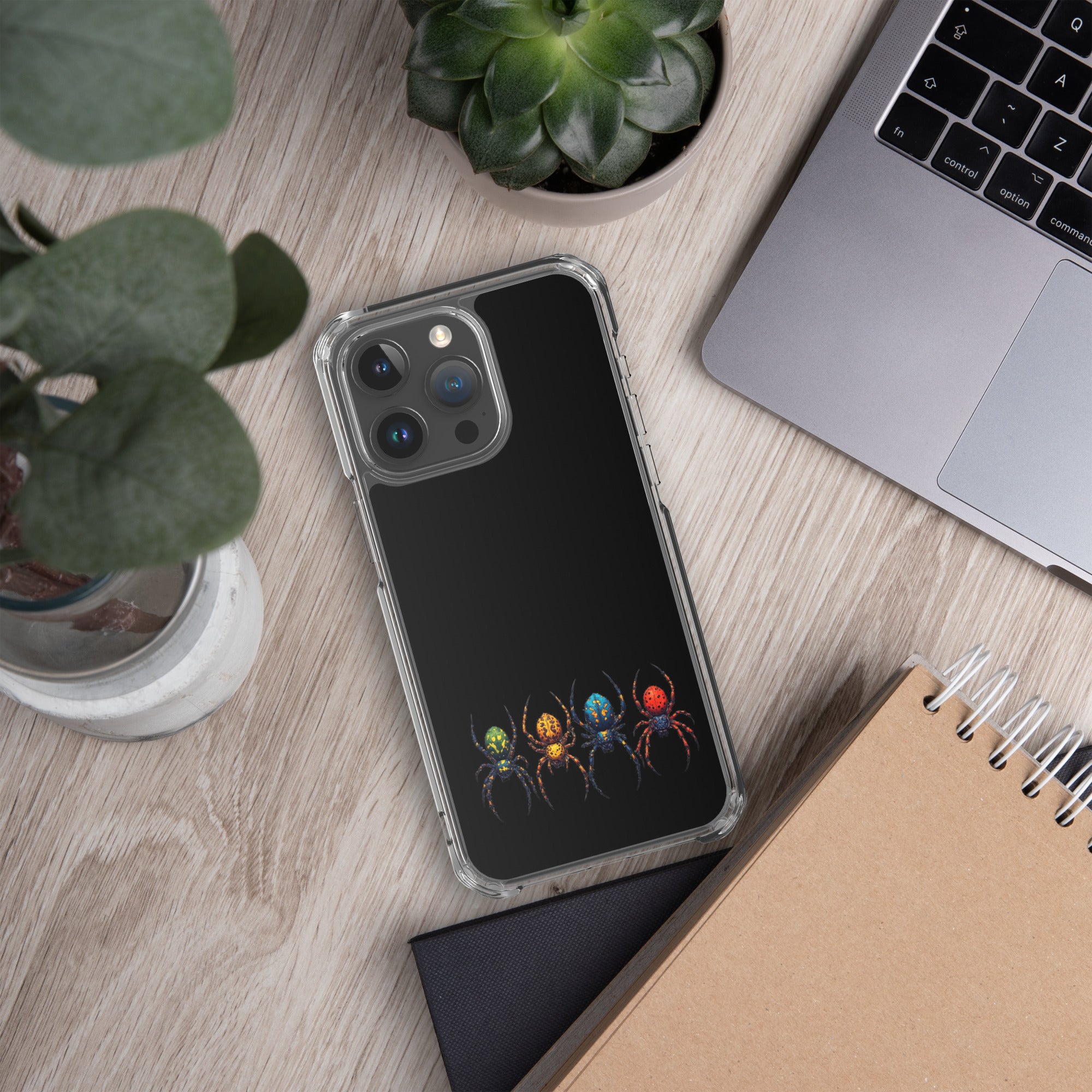 Phone case with spider design on a desk with laptop and plants