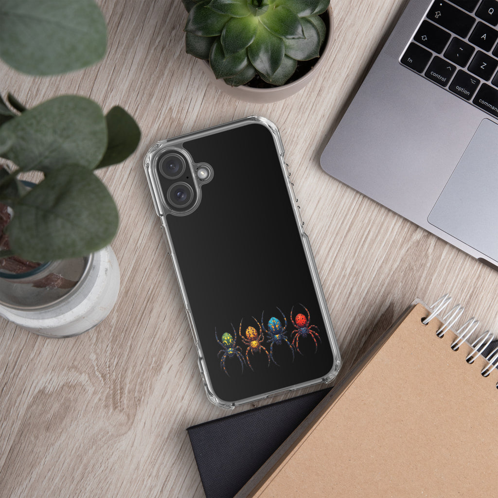 A clear-edged phone case with a black back featuring a colorful print of four stylized spiders in green, orange, yellow, and red, shown on a light wood desk with a laptop, notebook, and plants.