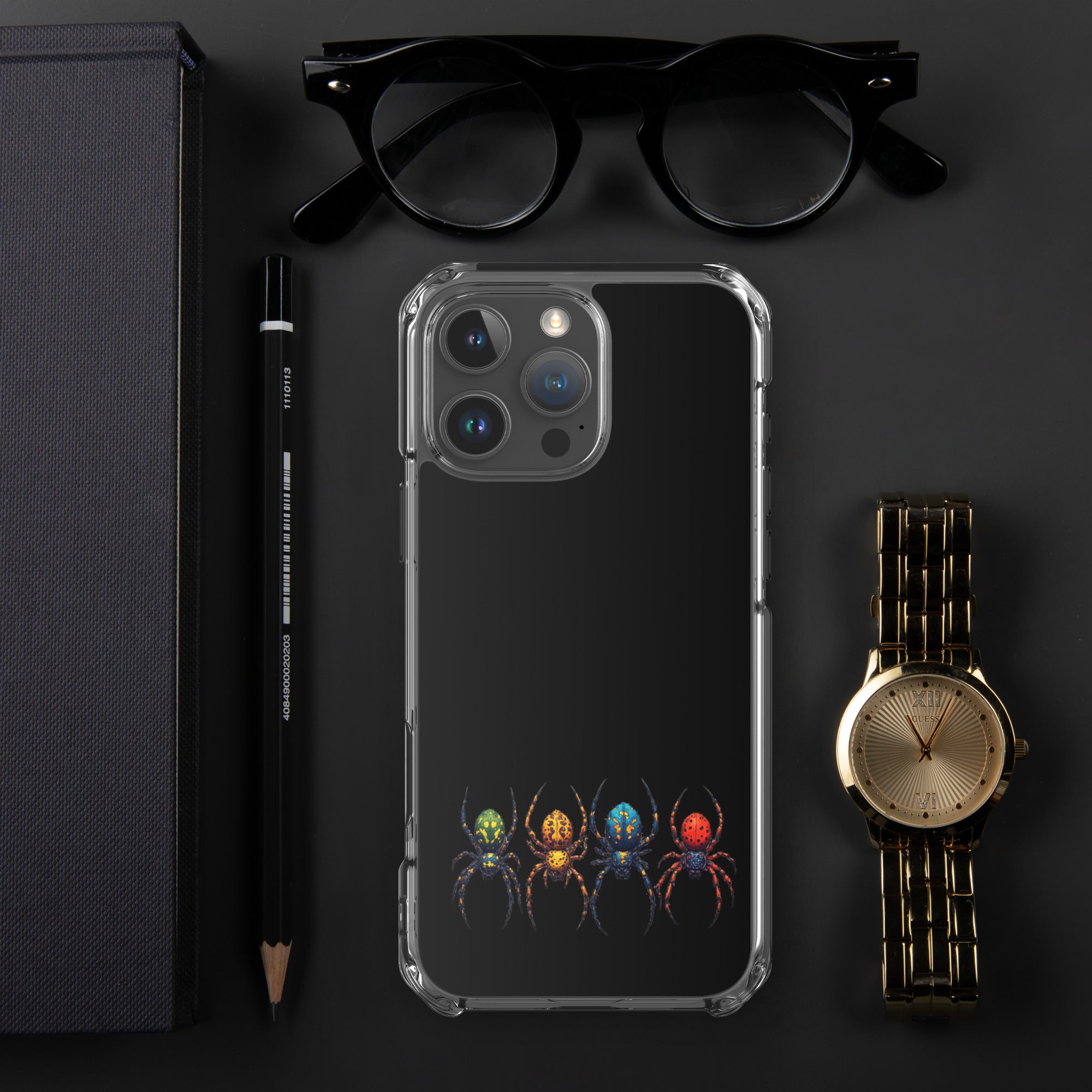 A clear protective phone case with a black back panel featuring a colorful graphic of four spiders at the bottom, styled in a flat-lay with black eyeglasses, a black pencil, a dark textured box, and a gold watch on a dark gray background.