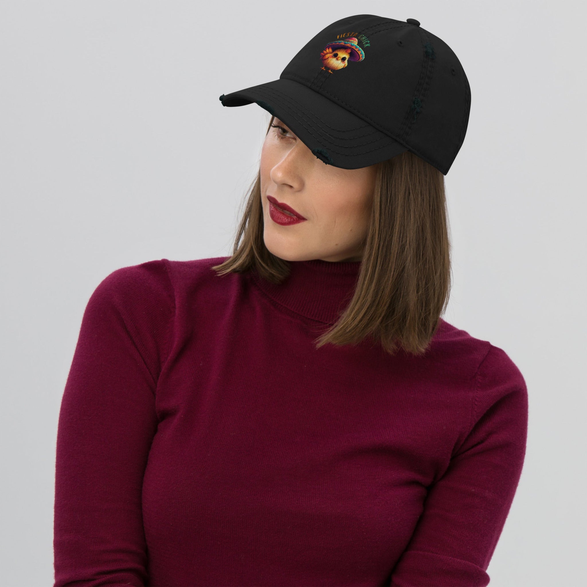 Woman wearing a black distressed dad hat with a cartoon chick wearing a sombrero and 'Fiesta Chick' text on a white background
