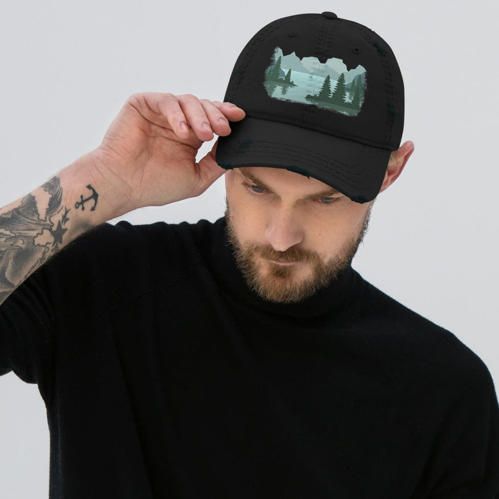 Man adjusting the bill of a black distressed graphic dad hat featuring a fisherman boat lake scene print, relaxed fit fishing cap with adjustable back closure. 