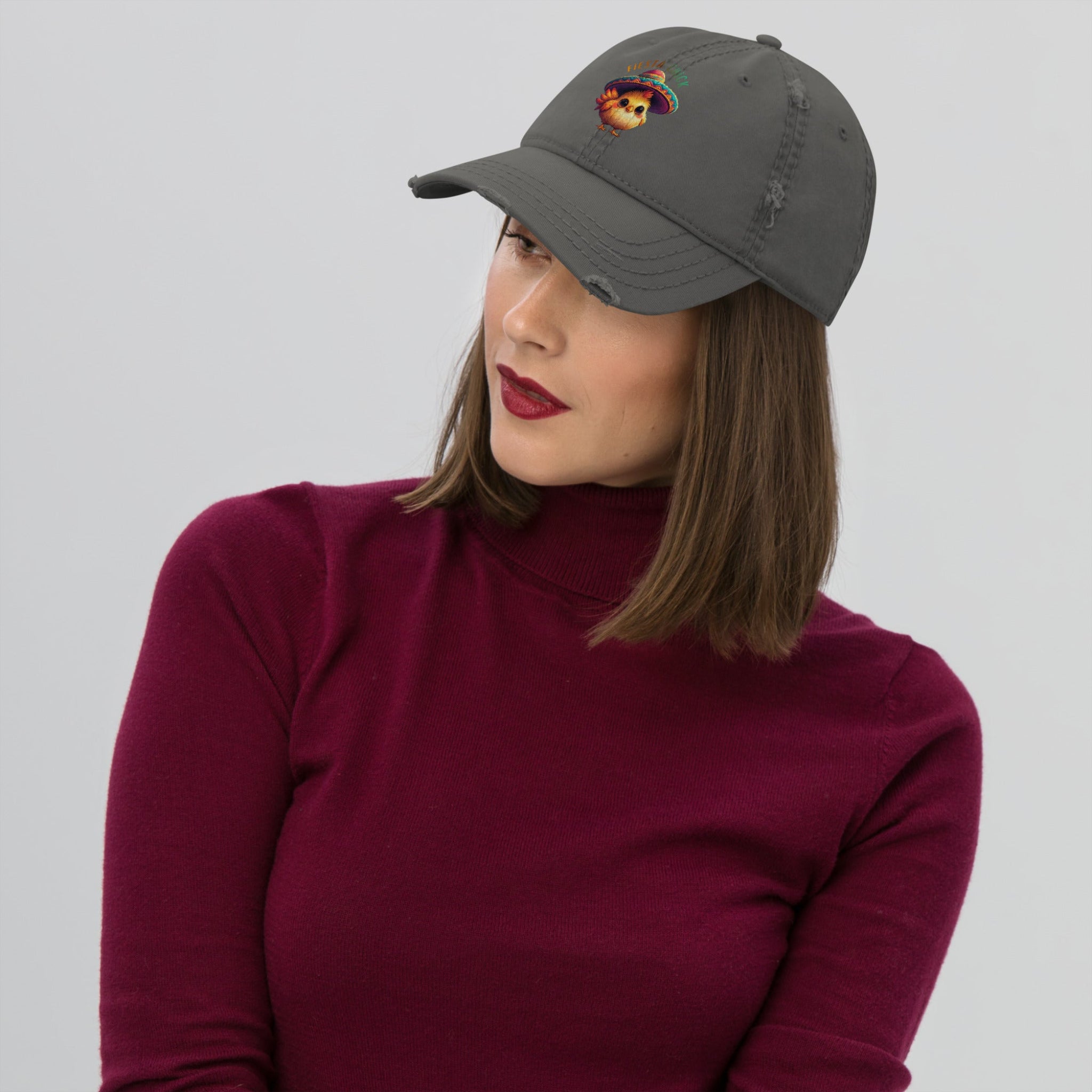 Woman wearing a grey distressed dad hat with a cartoon chick wearing a sombrero and 'Fiesta Chick' text on a white background