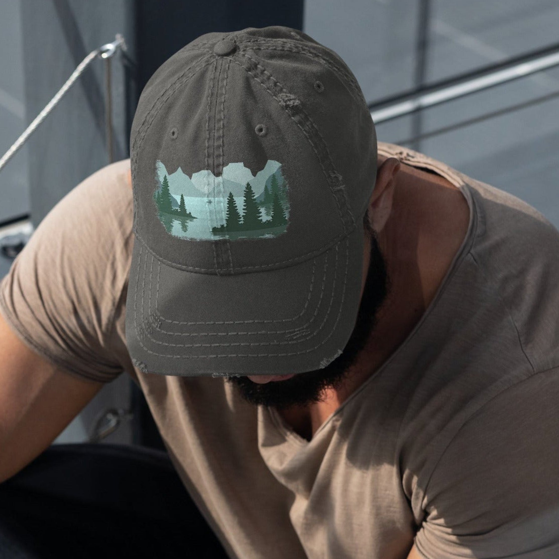 Man wearing a charcoal gray distressed dad hat with a fisherman lake scene graphic while out on a boat, casual outdoor fishing cap for men.