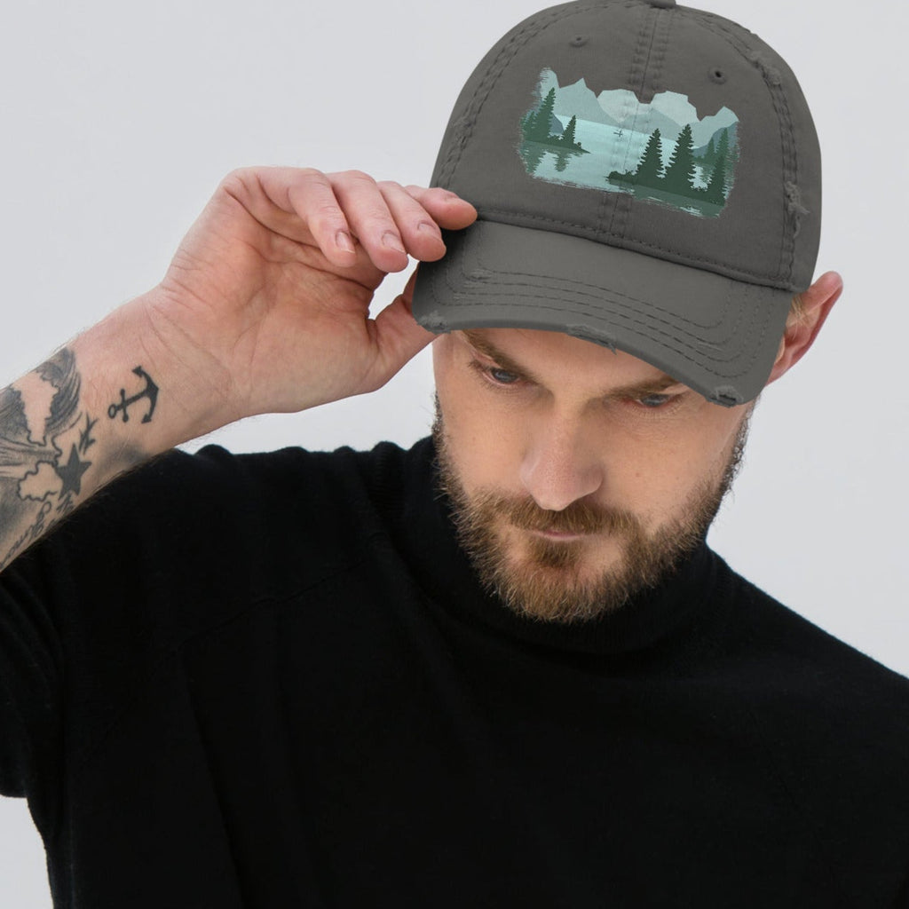 Man adjusting the bill of a charcoal gray distressed graphic dad hat featuring a fisherman boat lake scene print, relaxed fit fishing cap with adjustable back closure. 