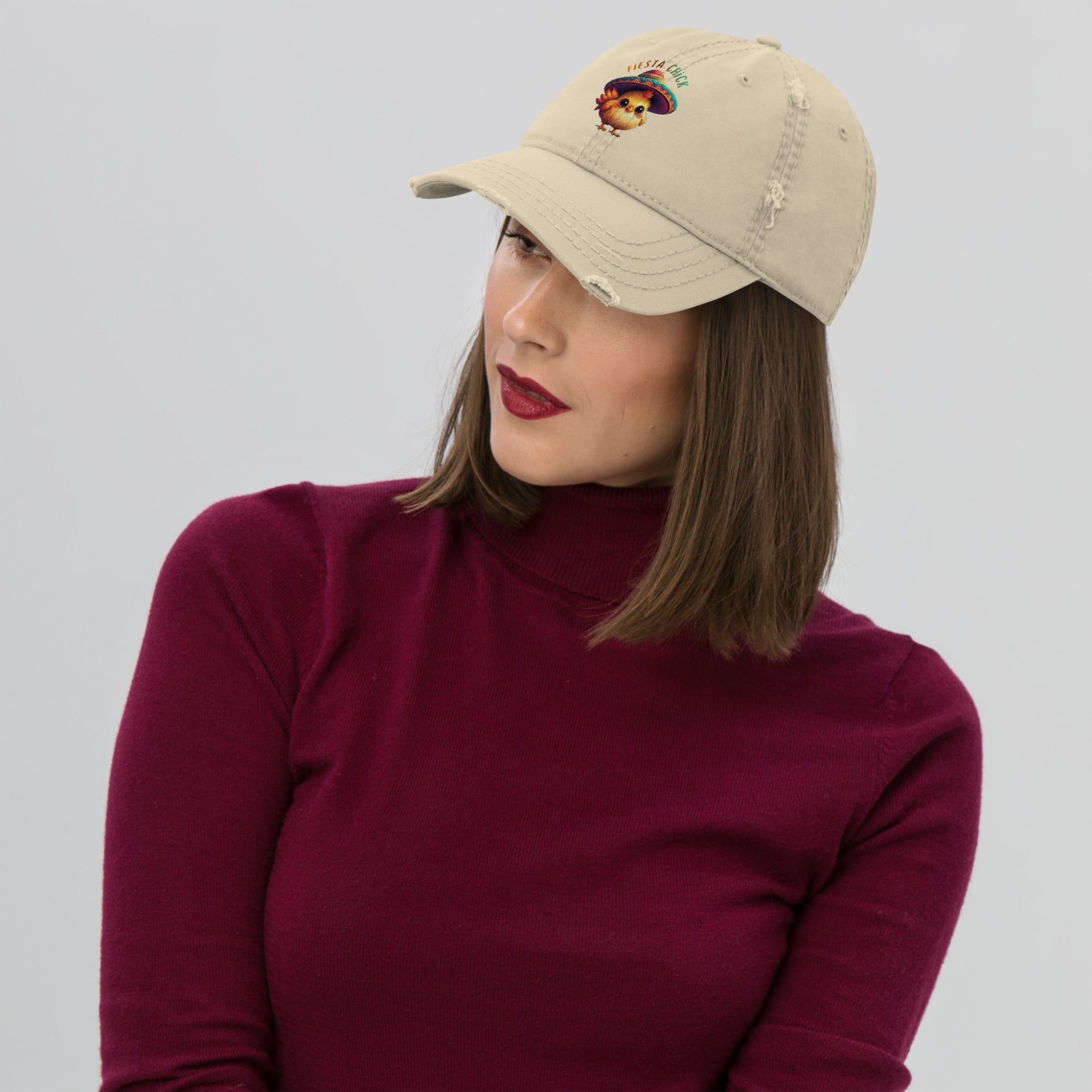 Woman wearing a beige distressed dad hat with a cartoon chick wearing a sombrero and 'Fiesta Chick' text on a white background