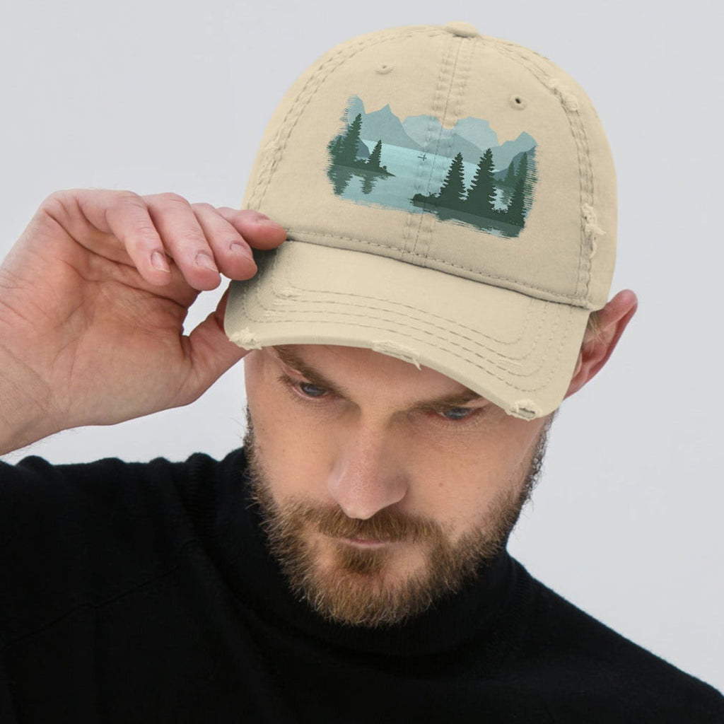 Man adjusting the bill of a tan distressed graphic dad hat featuring a fisherman boat lake scene print, relaxed fit fishing cap with adjustable back closure. 