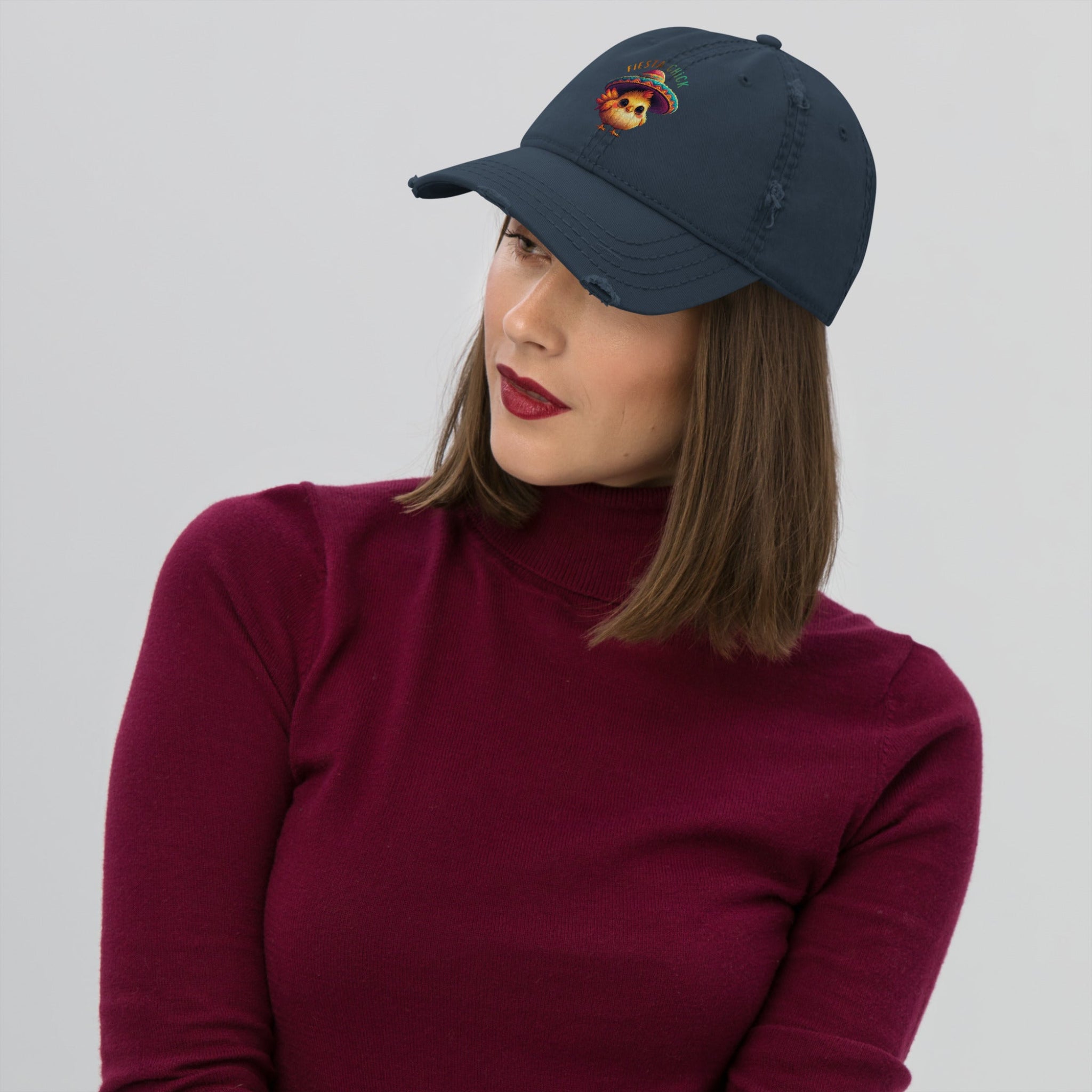 Woman wearing a navy blue distressed dad hat with a cartoon chick wearing a sombrero and 'Fiesta Chick' text on a white background