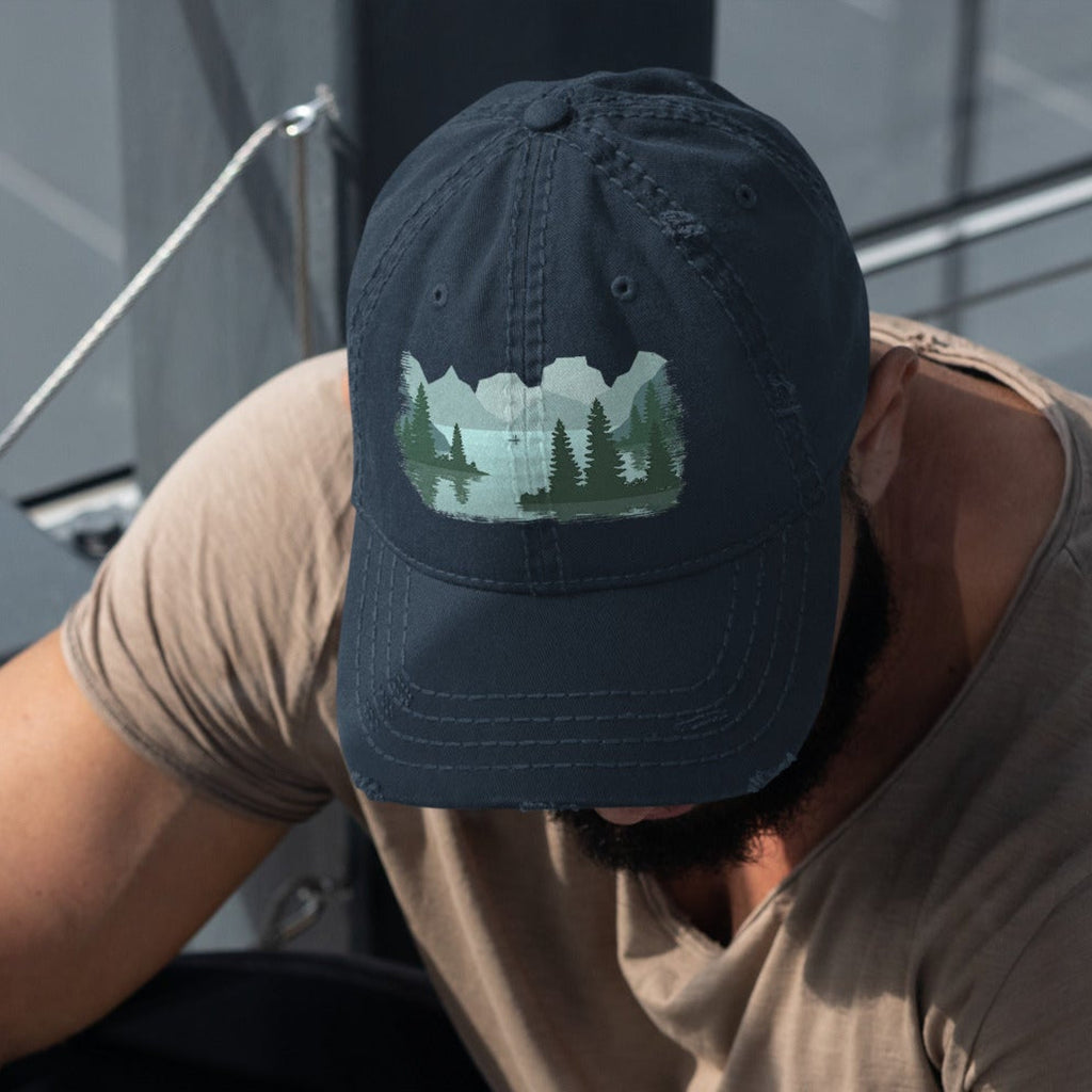 Man wearing a navy blue distressed dad hat with a fisherman lake scene graphic while out on a boat, casual outdoor fishing cap for men