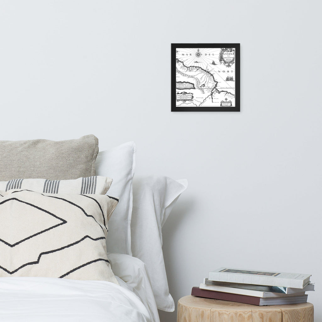 Framed map on a wall above a bed with pillows and books.
