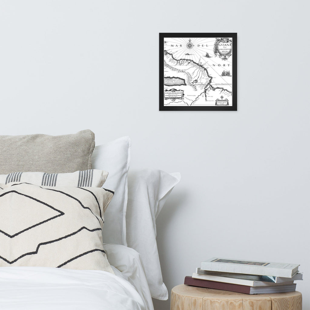 Framed map on a wall above a bed with pillows and books.