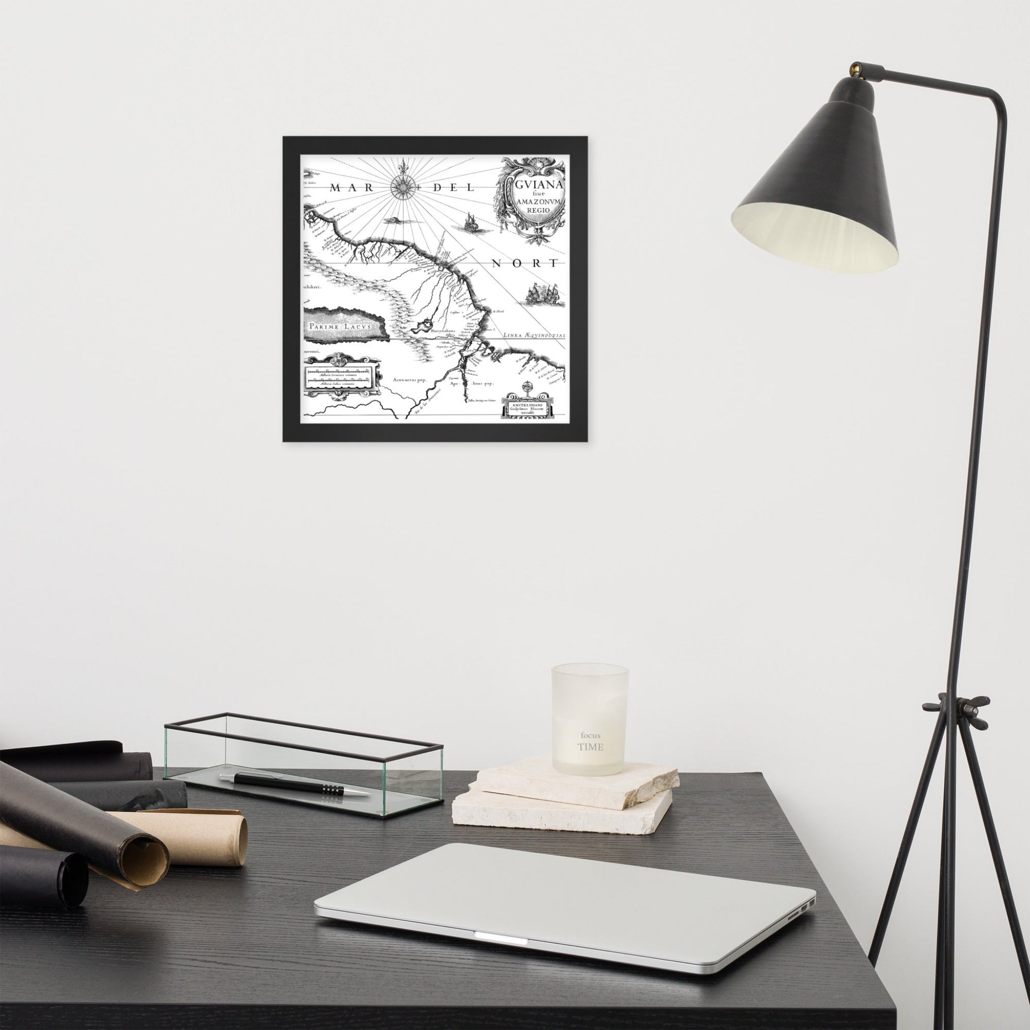 Framed map on a wall above a desk with a laptop and lamp.