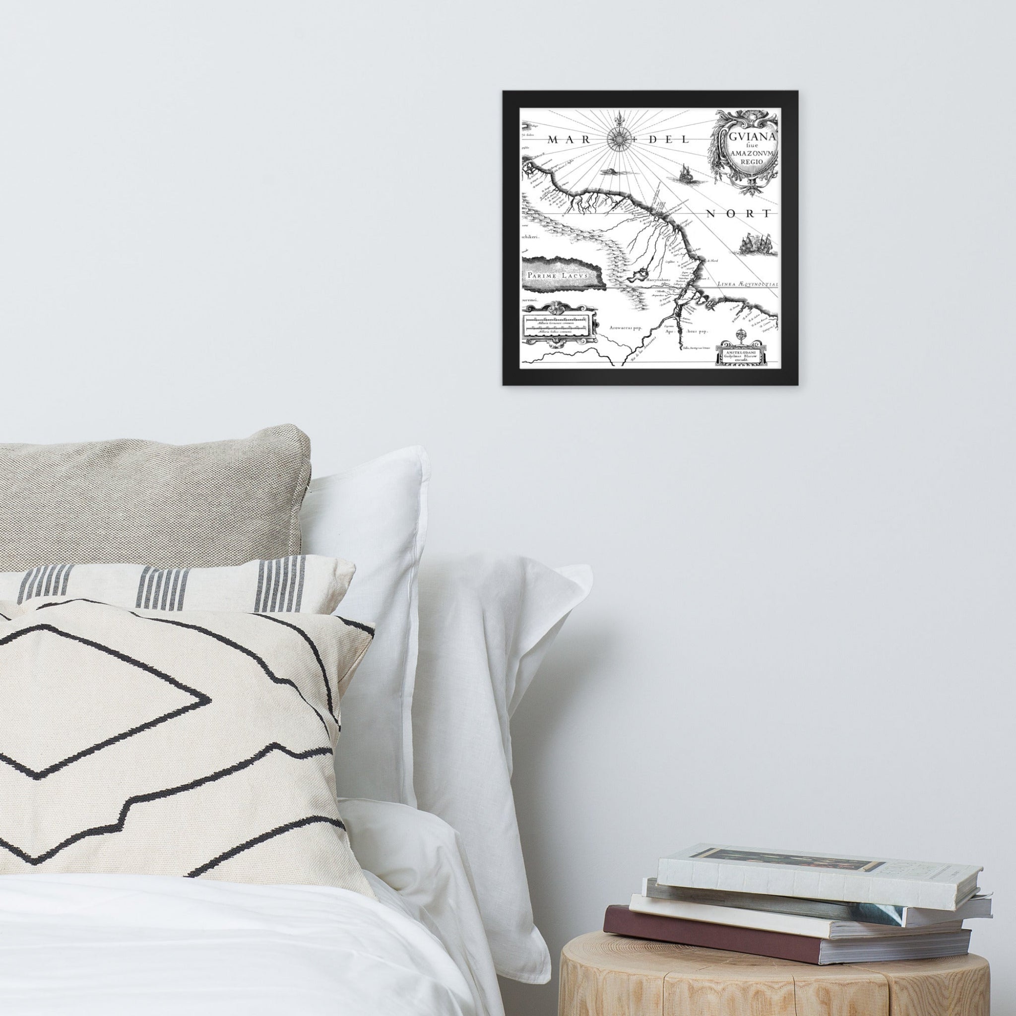 Framed map on a wall above a bed with pillows and books.