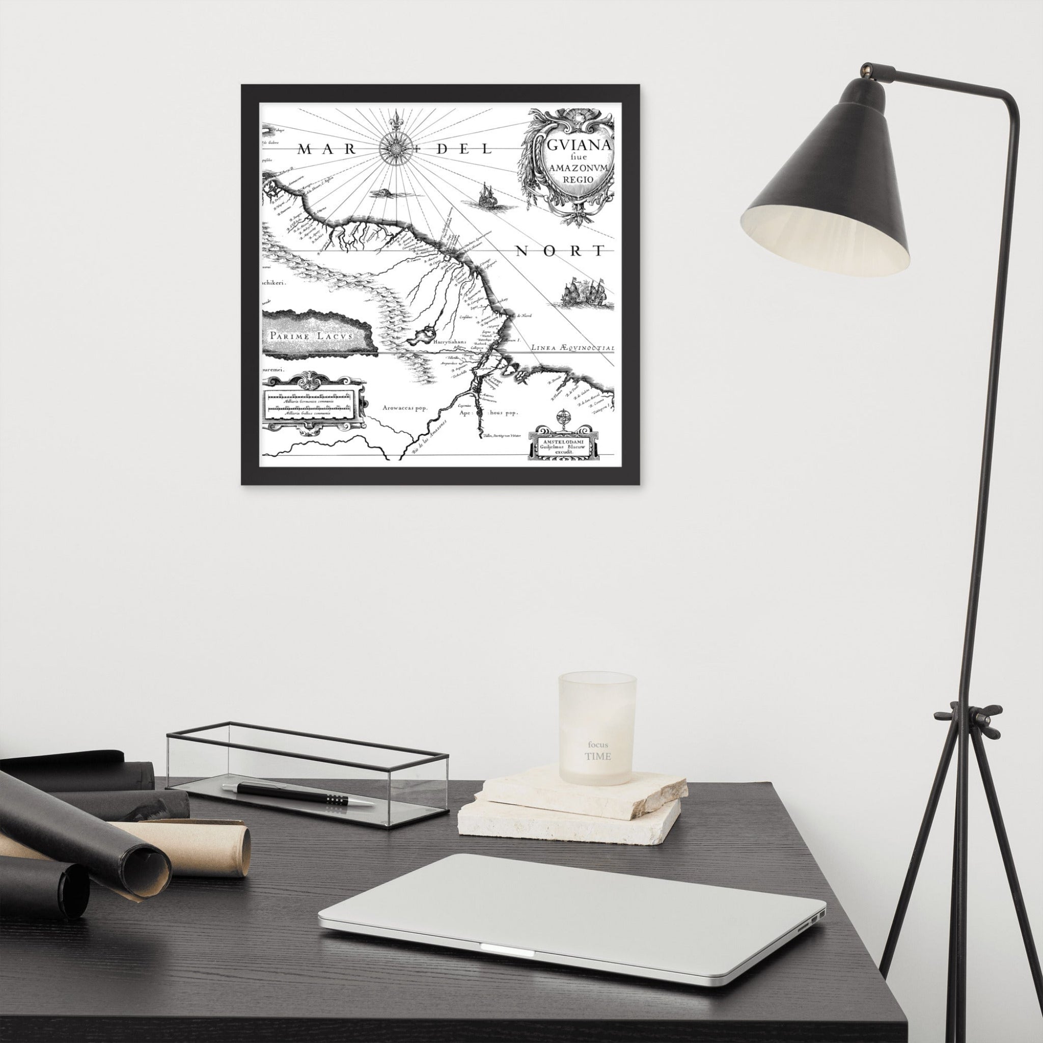 Framed black and white map on a wall above a desk with a laptop and lamp.