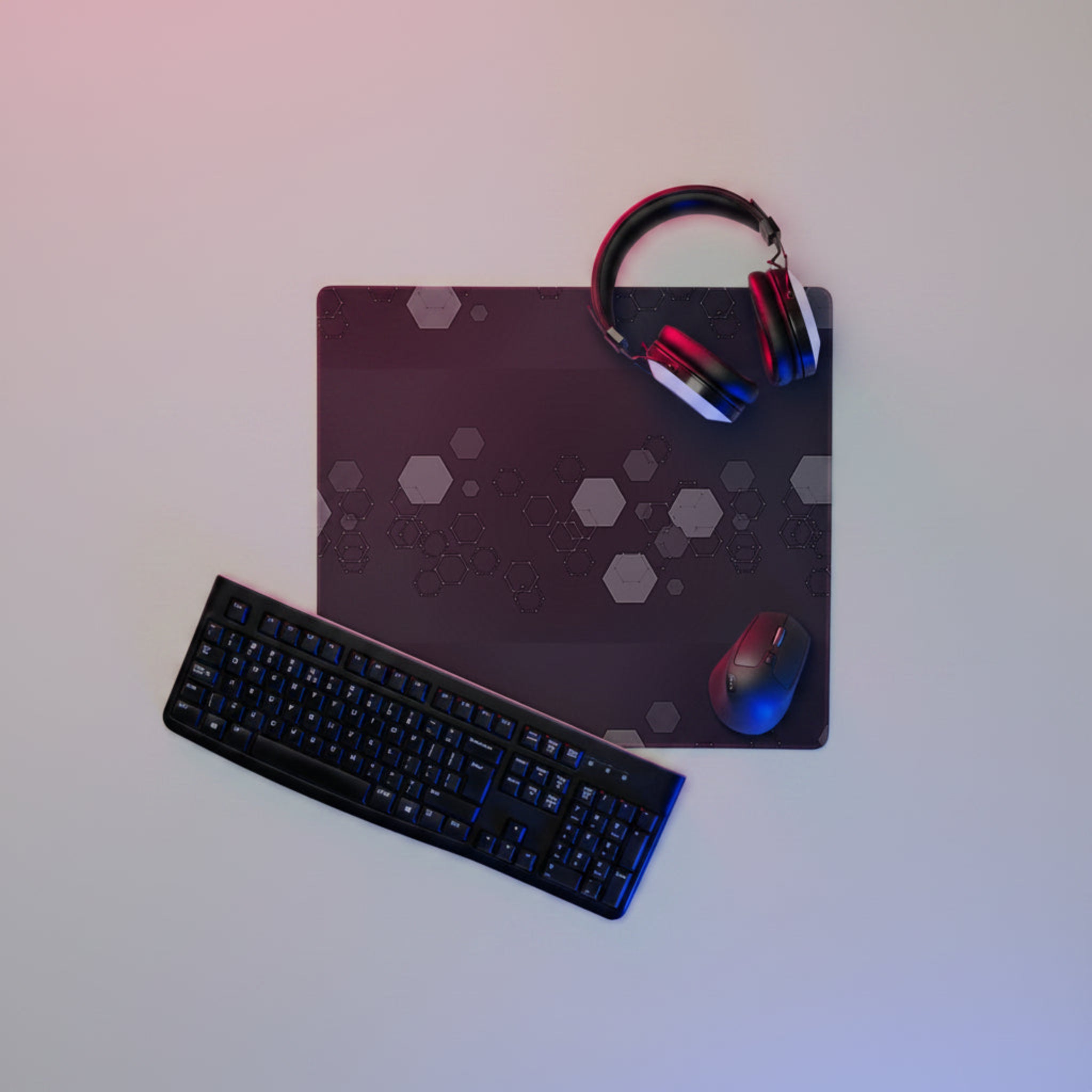Headphones and keyboard laying on a Dark extended gaming desk mat with grey hexagon geometric pattern. 