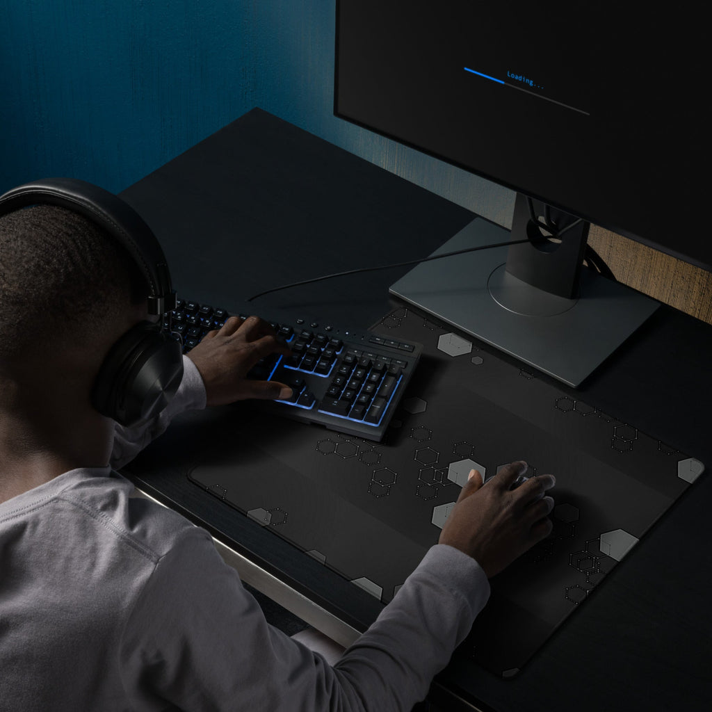 Person wearing headphones using a computer with a Dark extended gaming desk mat with grey hexagon geometric pattern. 